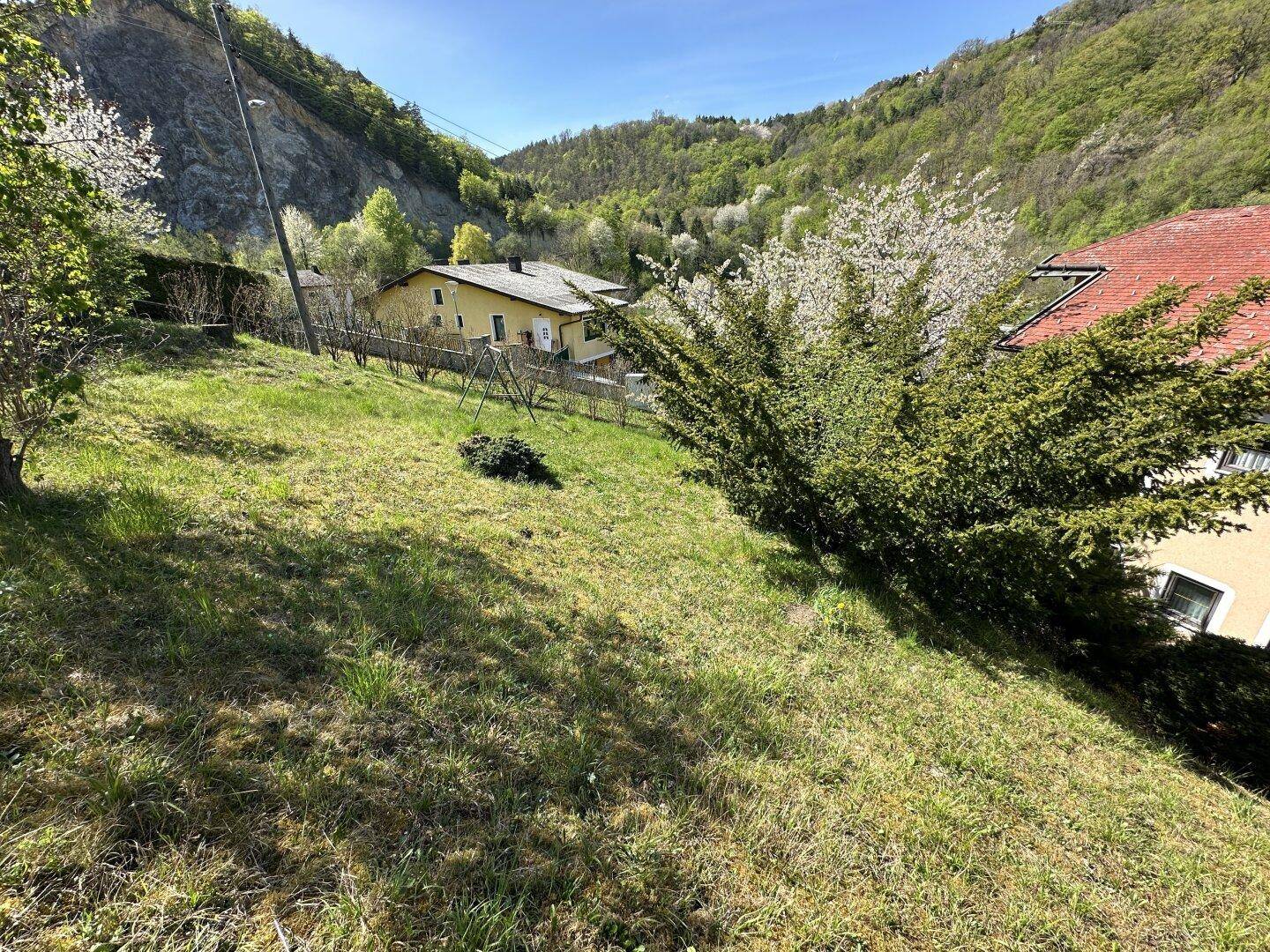 Hanglage des Gartens mit Rasenfläche und Blick auf umliegende Häuser und grüne Hügel.