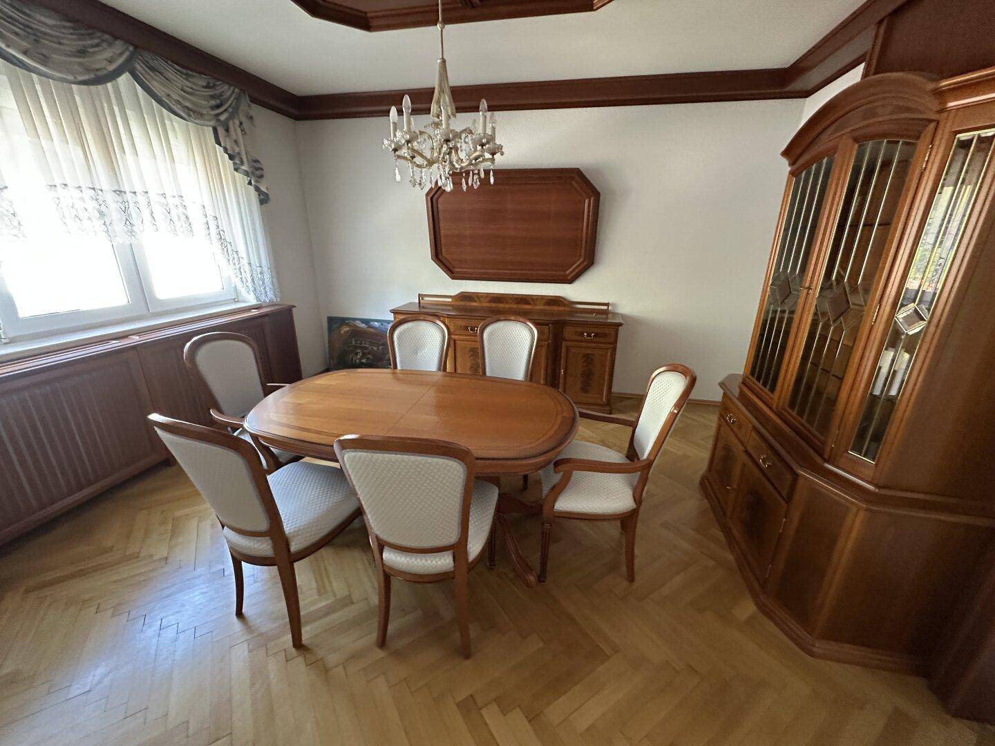 Klassisches Esszimmer mit ovalem Holztisch, passenden Stühlen und Fischgrätparkettboden.