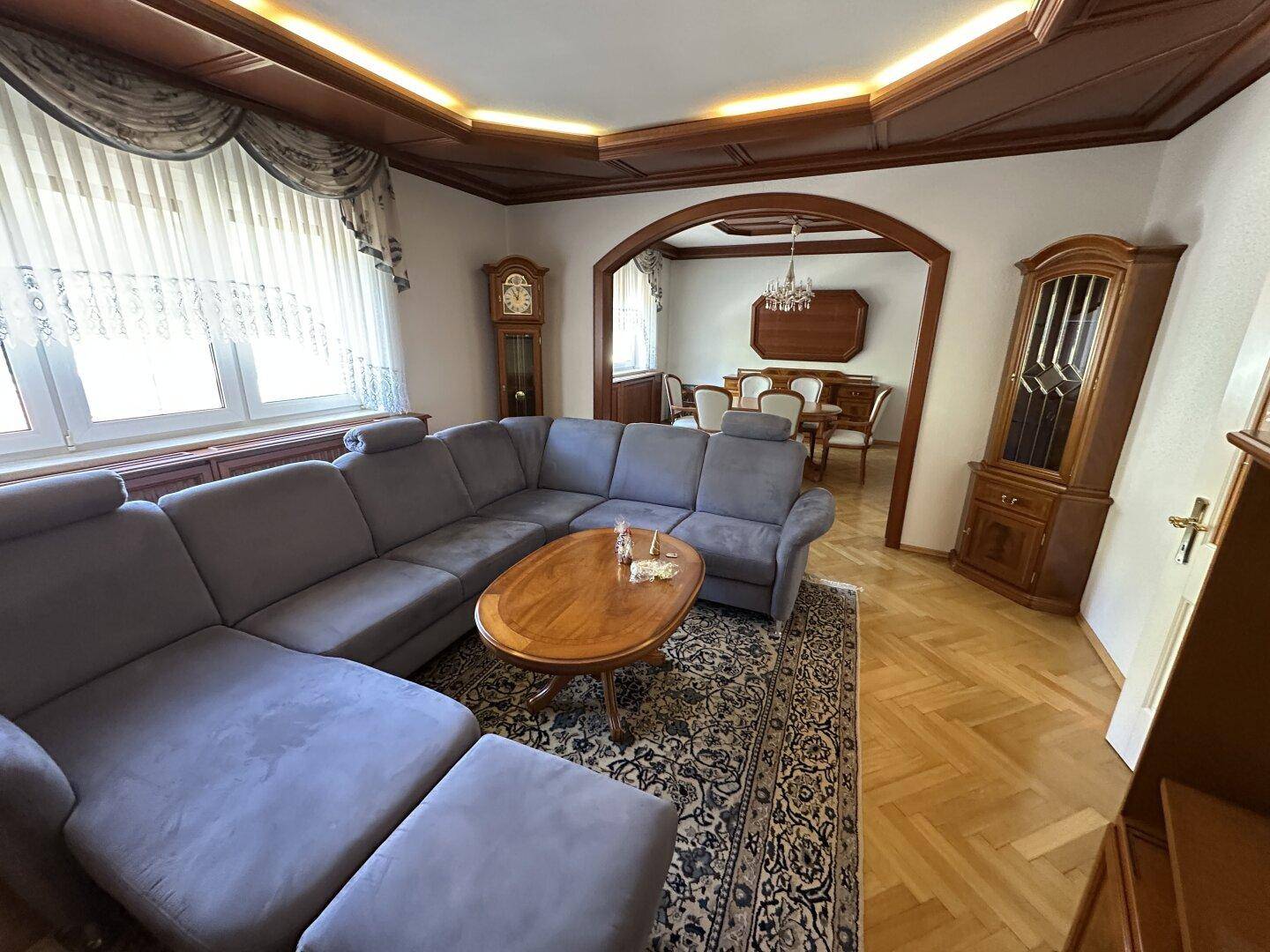 Gemütliches Wohnzimmer mit großem Ecksofa, Fischgrätparkett und einer aufwendigen Holzdecke.