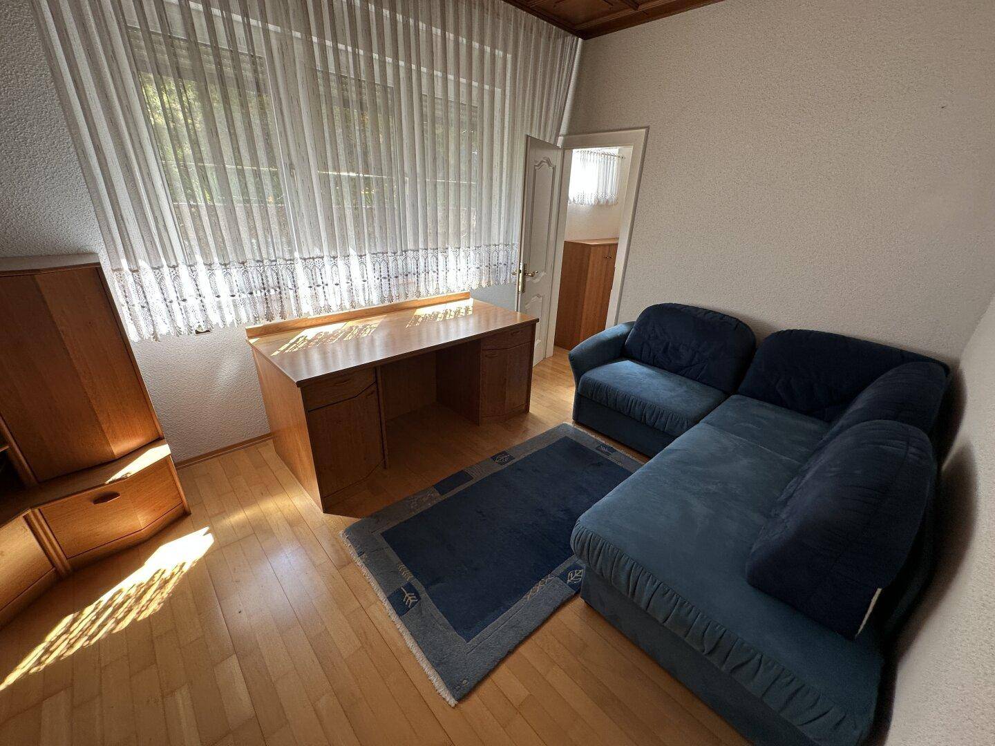 Helles Arbeitszimmer mit Holzschreibtisch, blauem Sofa und Parkettboden.
