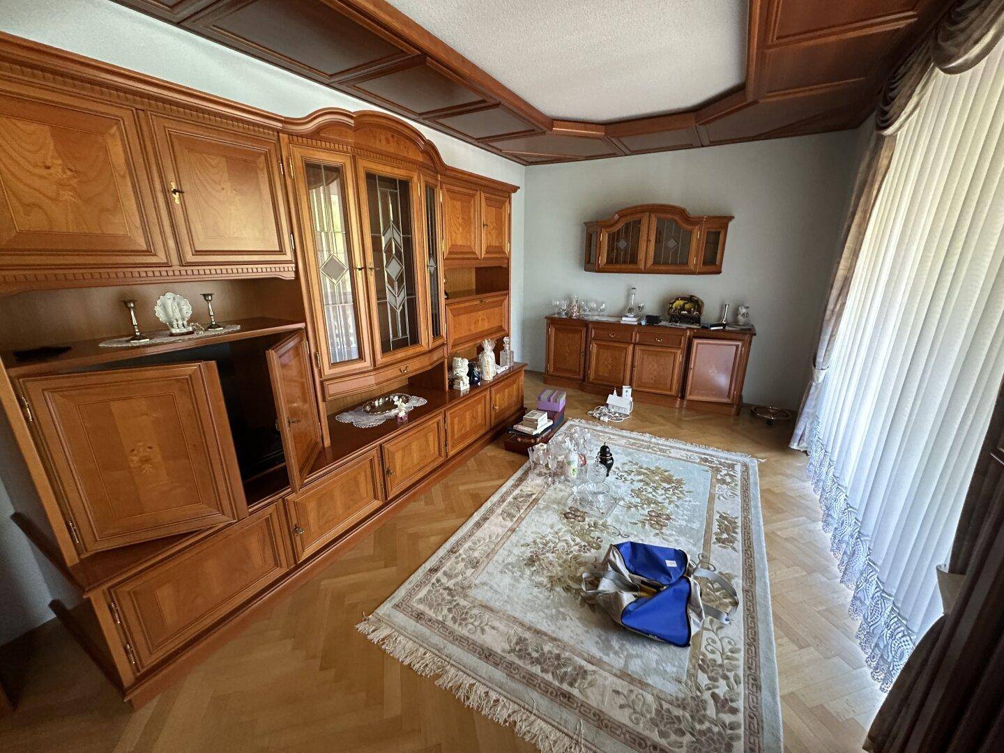 Wohnzimmer mit großer Holzschrankwand, Fischgrätparkett und traditioneller Deckenverkleidung.