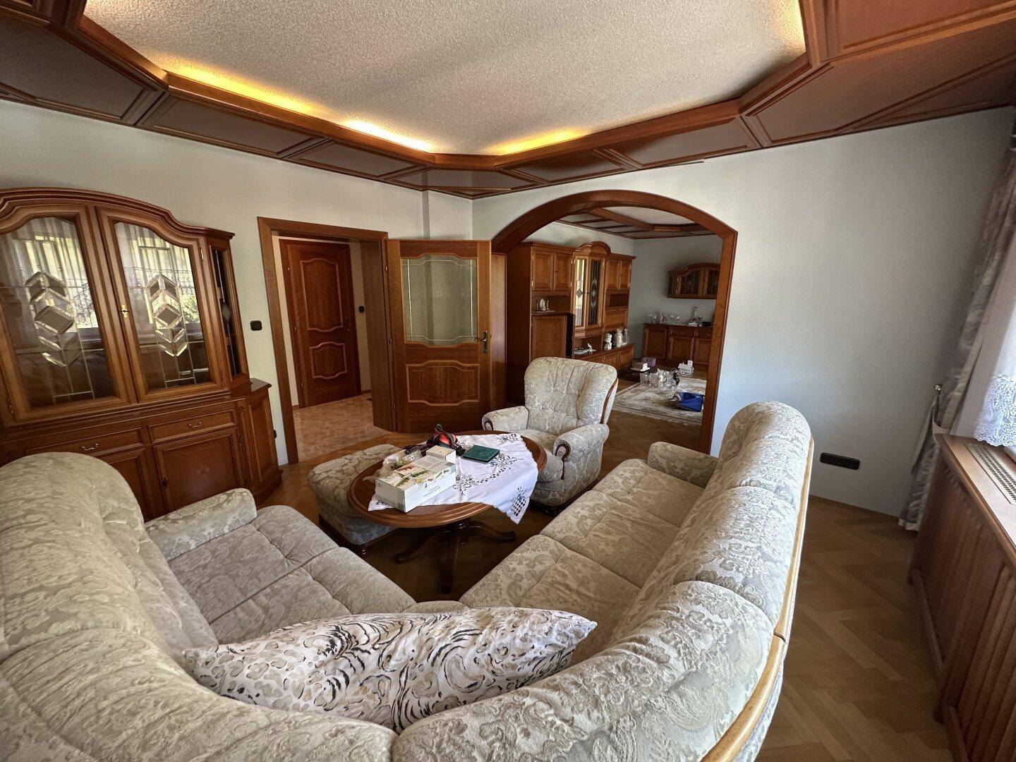 Geräumiges Wohnzimmer mit traditionellen Möbeln, Parkettboden und Zugang zu weiteren Räumen.