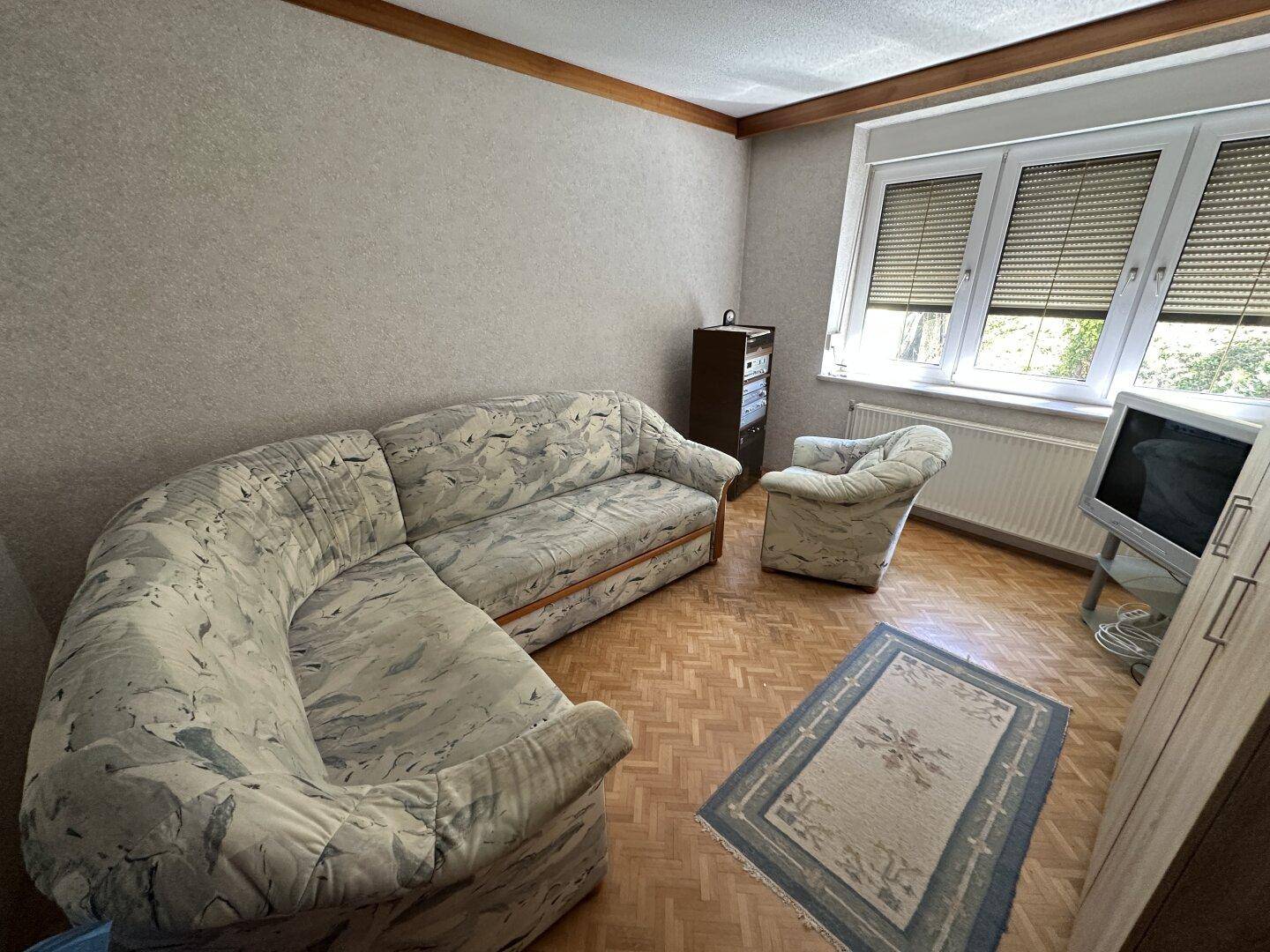 Einfaches Zimmer mit Sofa, Fernseher und Parkettboden, ideal als Gästezimmer.