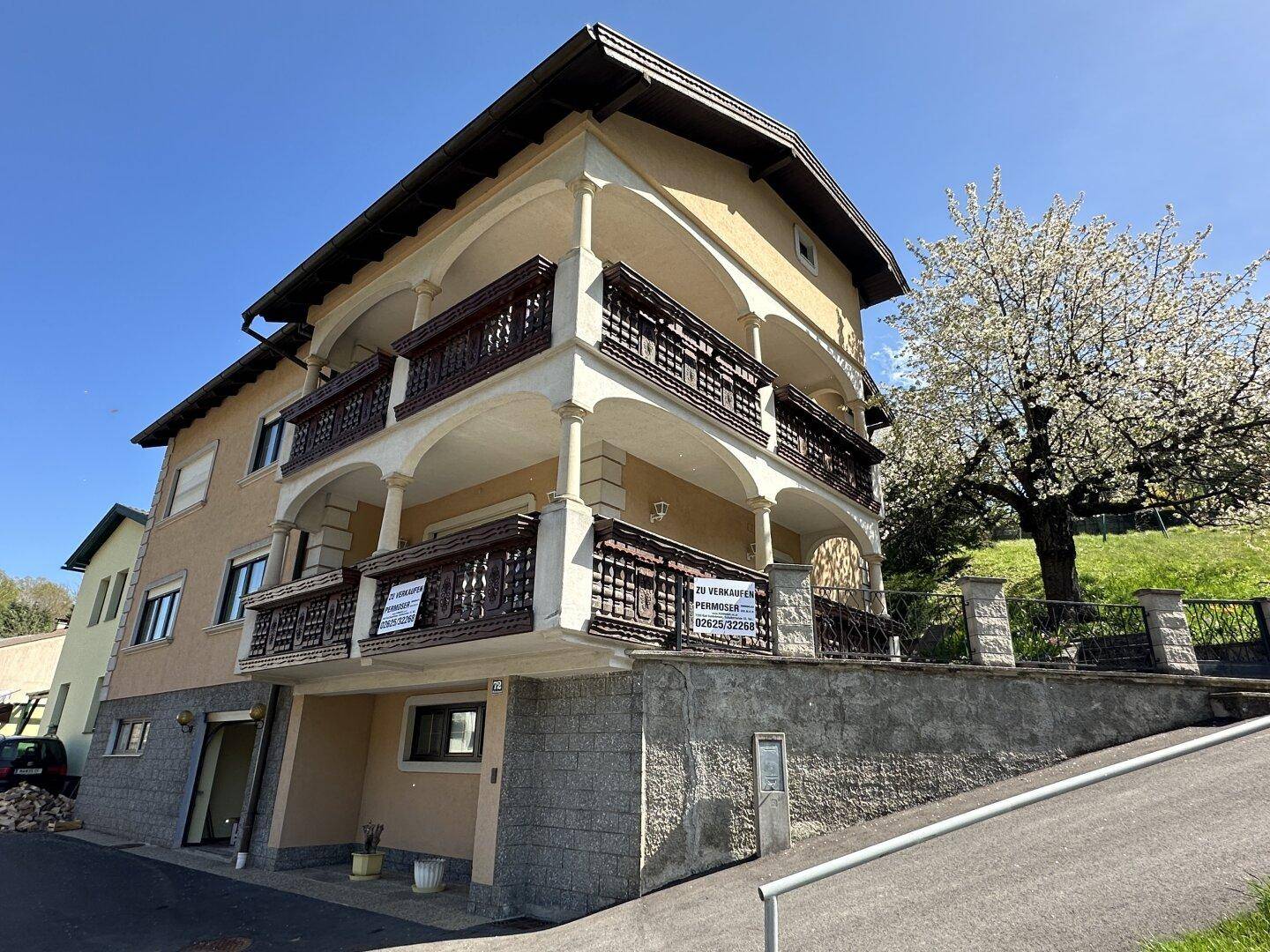 Seitenansicht des Wohnhauses mit Balkonen und traditioneller Architektur, umgeben von grüner Landschaft.