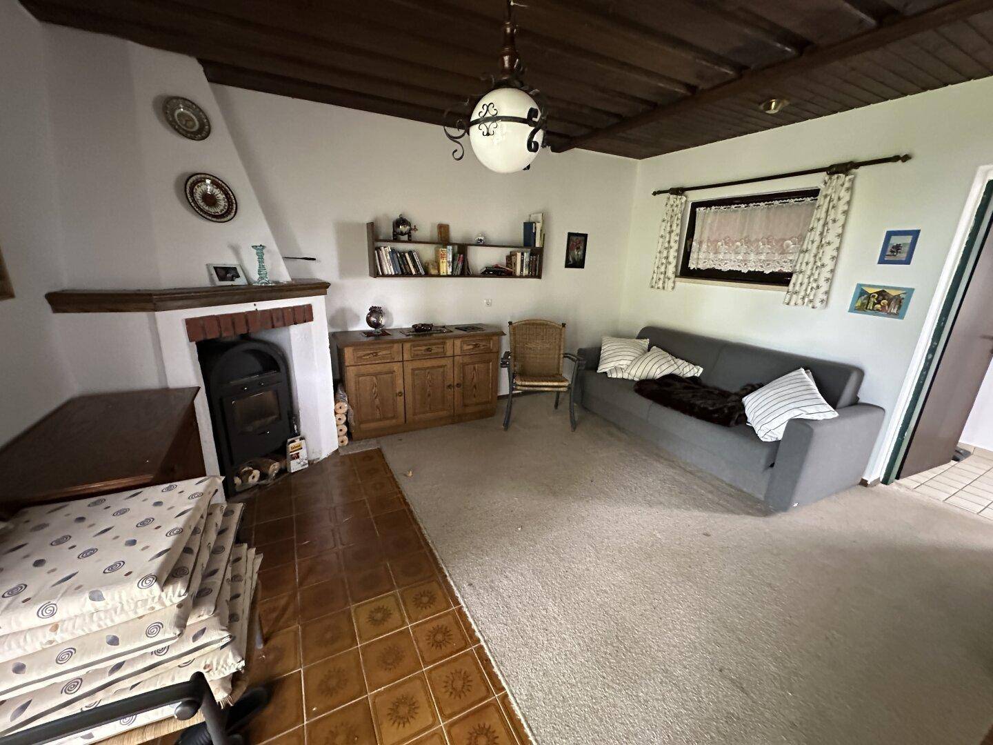 Gemütliches Wohnzimmer mit Kamin, Teppichboden und rustikaler Holzbalkendecke.