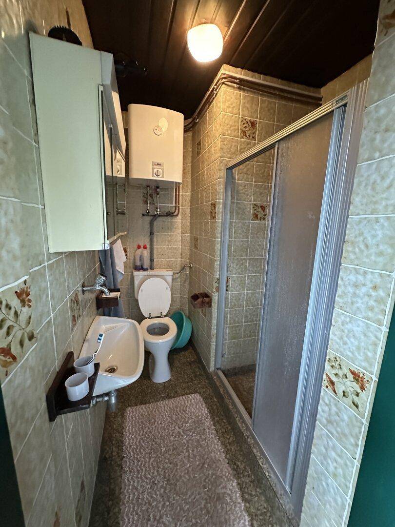 Kleines Badezimmer mit Dusche, WC, Waschbecken und beigefarbenen Fliesen im 80er-Jahre-Stil.