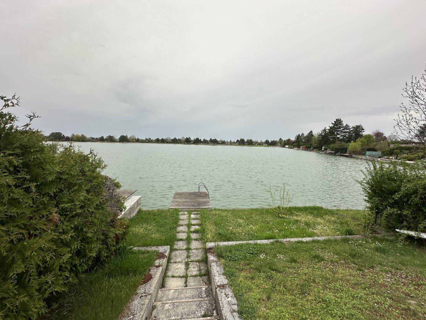 Gartenbereich mit Steintreppe und Blick auf den See mit einem Badesteg.