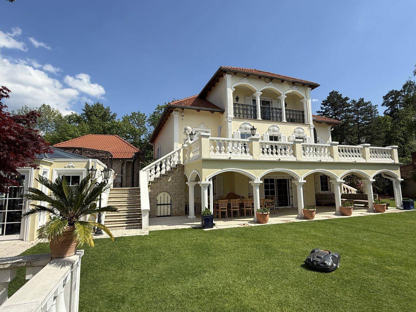 Elegante Villa mit weitläufigem Rasen, überdachter Terrasse und klassischer Architektur unter blauem Himmel.