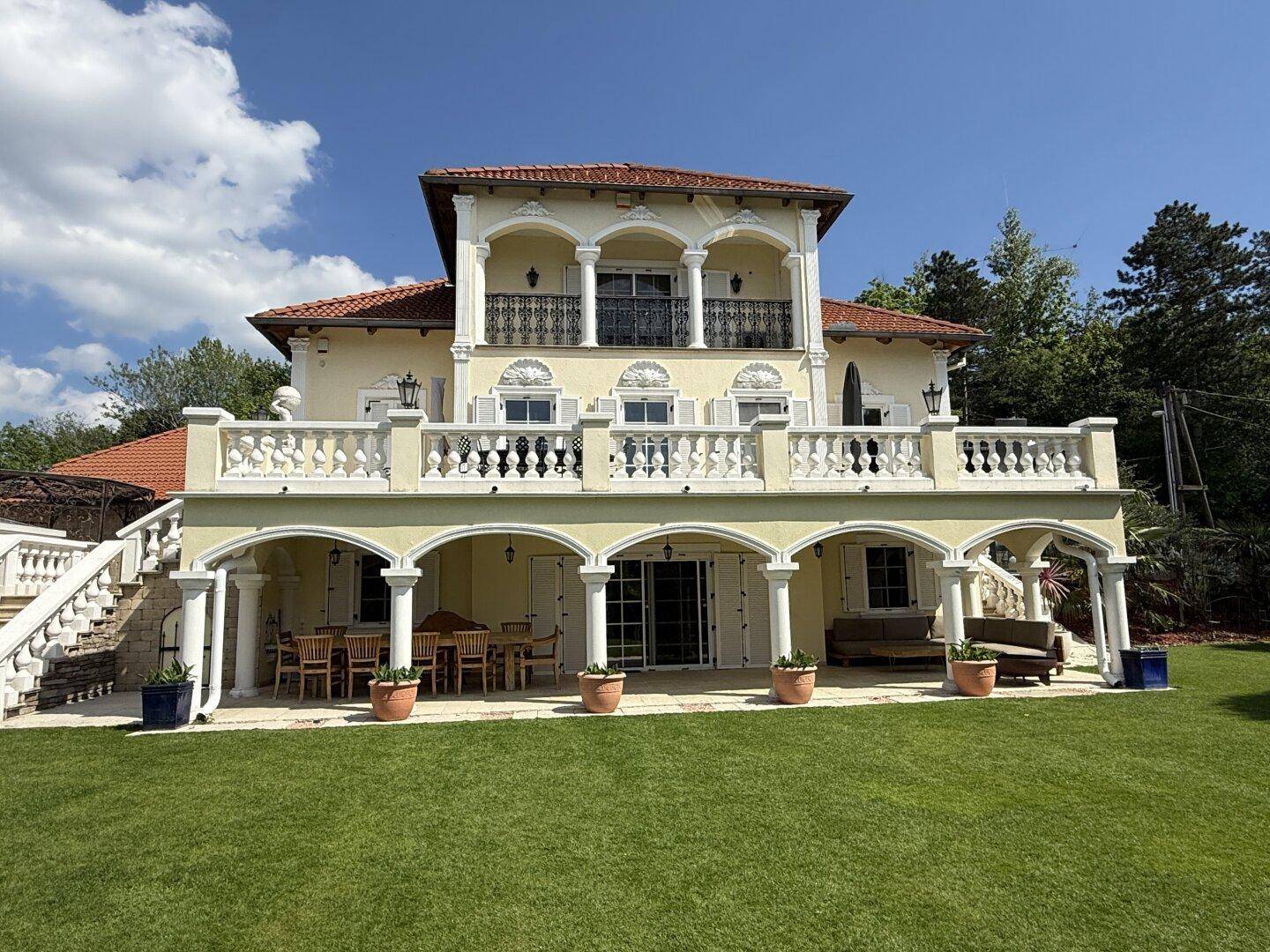 Elegante Villa mit gepflegtem Rasen, großer Terrasse und klassischer Architektur im Sonnenlicht.