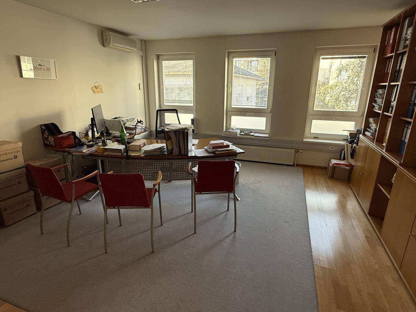 Funktional eingerichtetes Büro mit Schreibtisch, Bürostühlen, Bücherregalen und Klimaanlage.