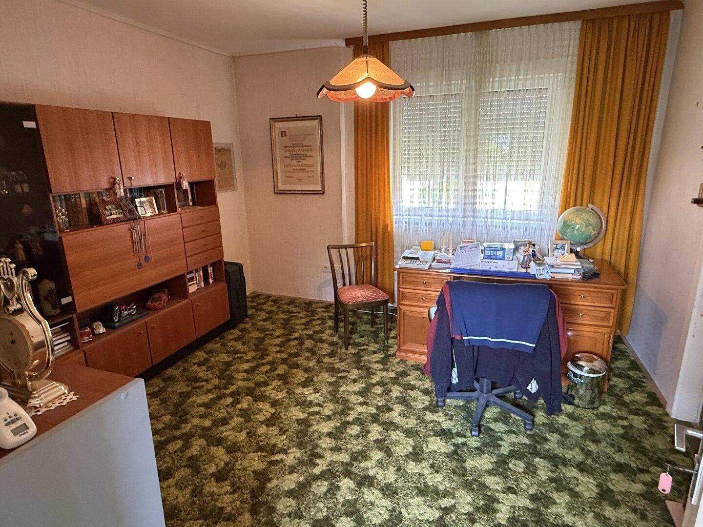 Arbeitszimmer mit Schreibtisch, Holzregal und gemustertem Teppichboden in grünen Tönen.