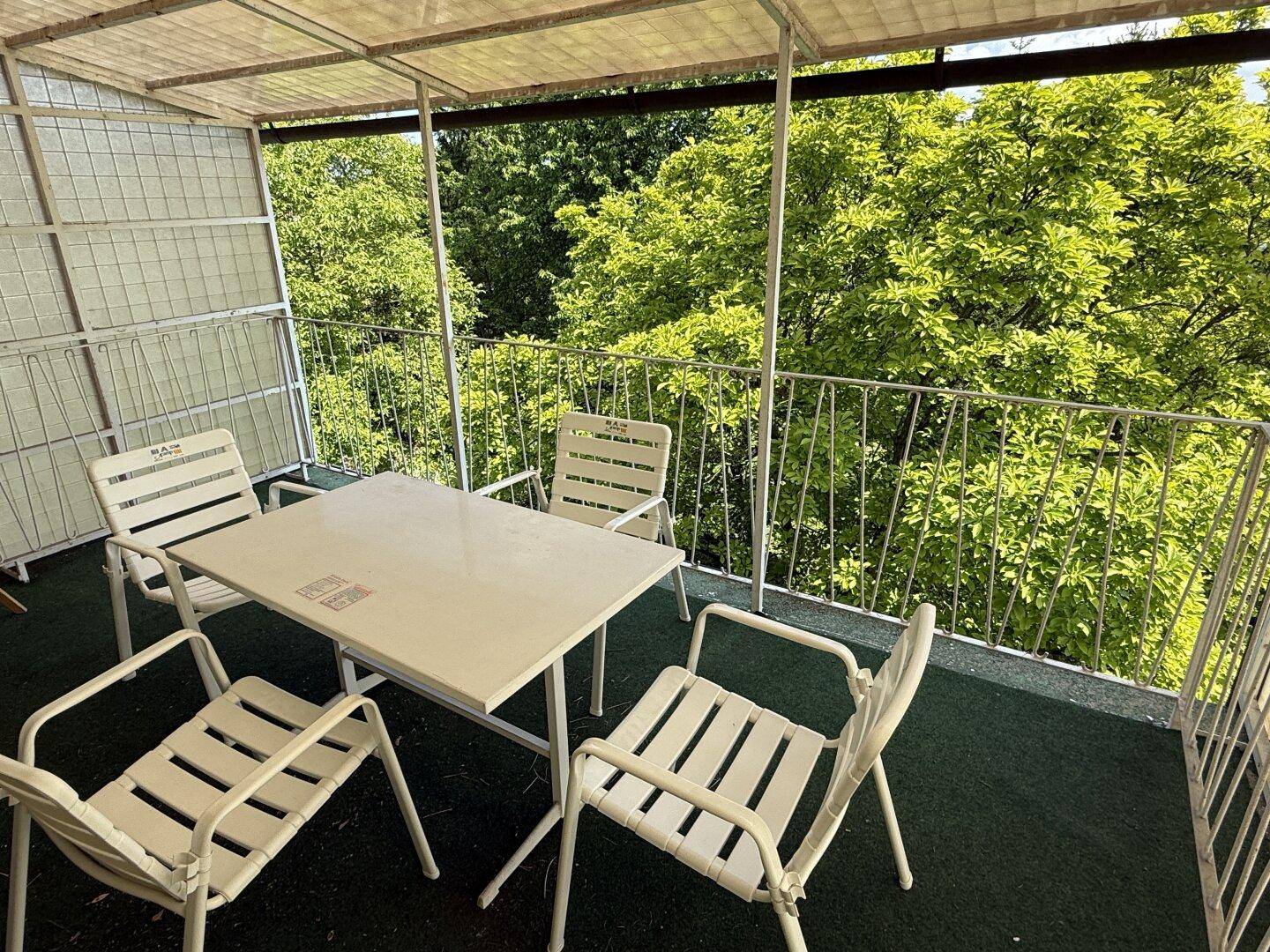 Überdachter Balkon mit Gartenmöbeln und weitem Blick auf die umliegenden Bäume.