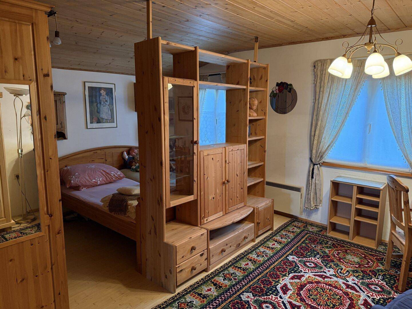 Schlafzimmer mit Holzbett, großem Holzregal und gemustertem Teppichboden.