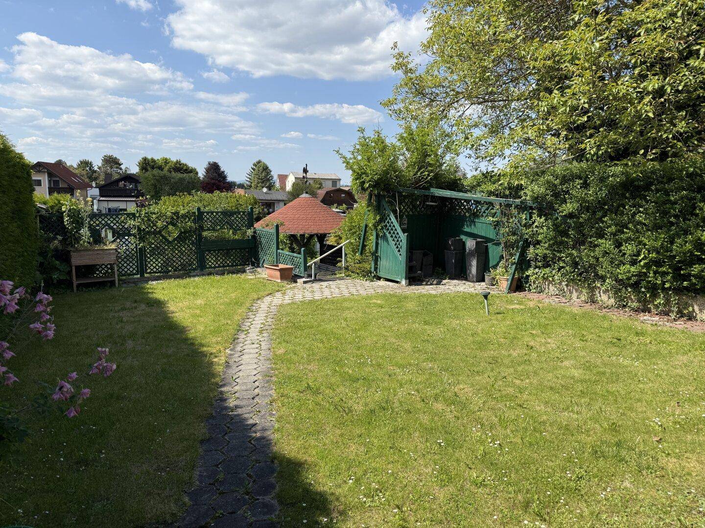 Gepflegter Garten mit Rasenfläche, Steinweg und einem kleinen Gartenhaus.