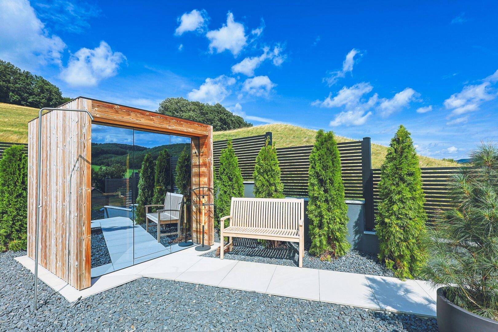 Ruhiger Gartenbereich mit Sitzbank, Zierbäumen und moderner Glasstruktur.