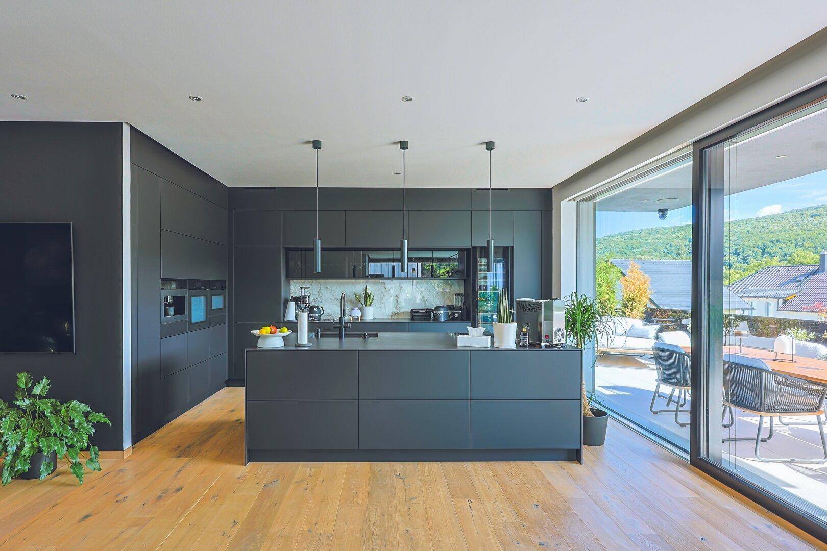 Elegante schwarze Küche mit Kochinsel und großen Schiebetüren zur Terrasse.