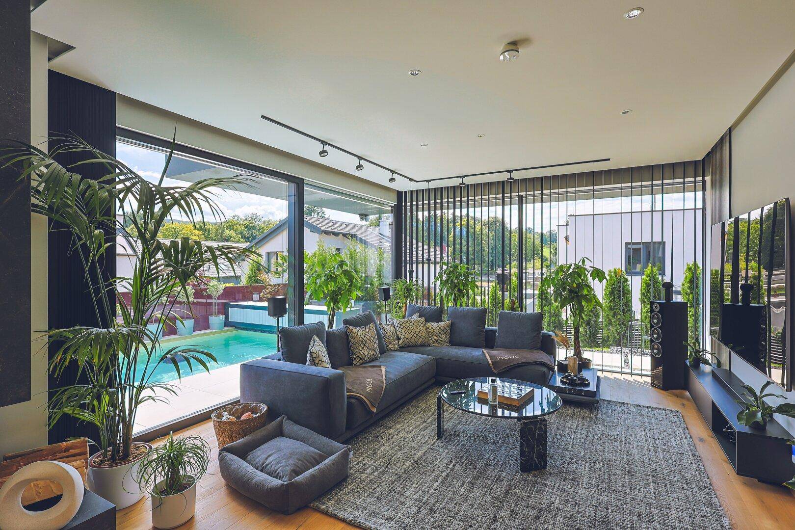 Gemütliches Wohnzimmer mit großem Sofa, vielen Pflanzen und Blick auf den Pool.