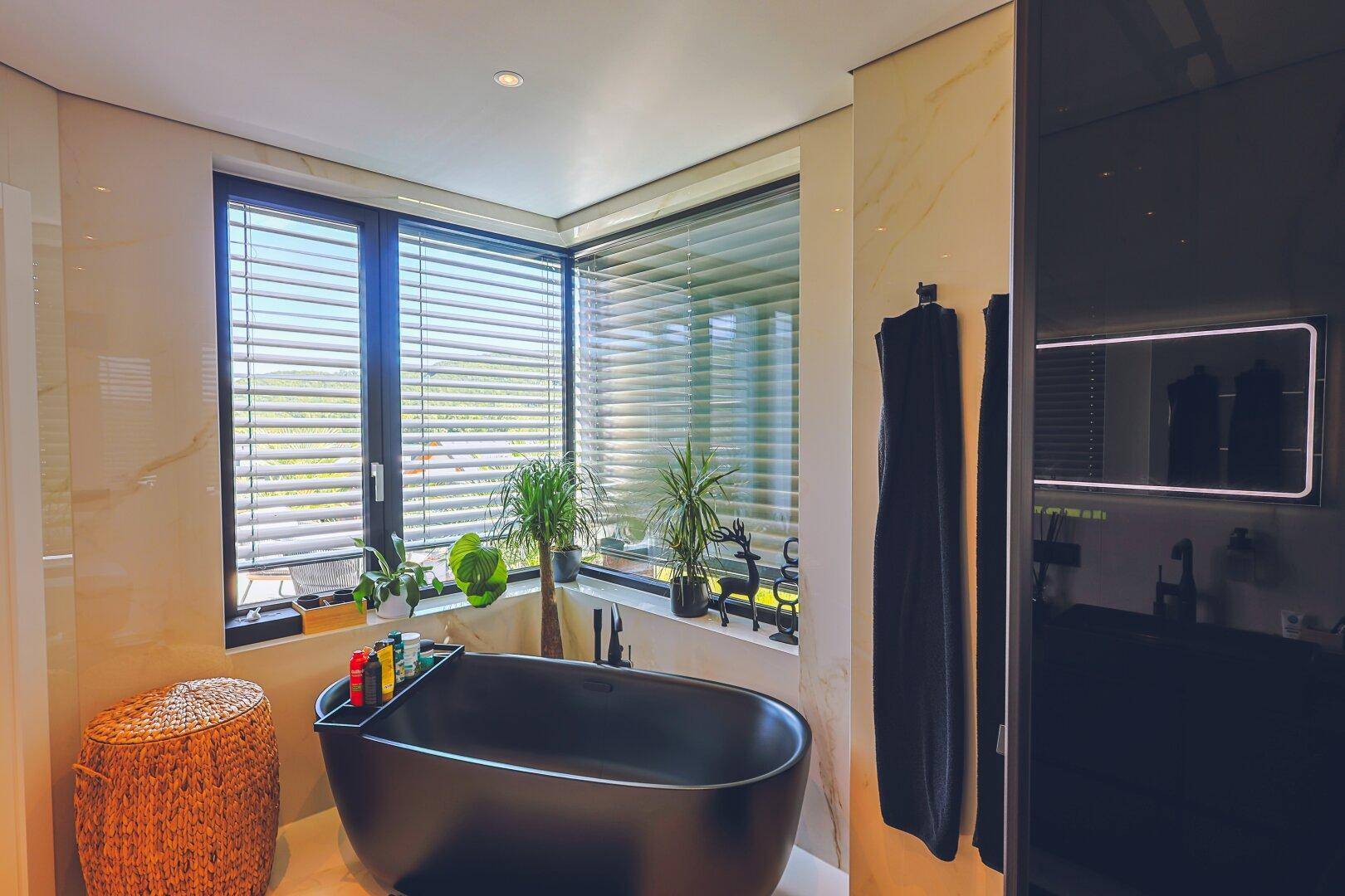 Luxuriöses Badezimmer mit freistehender schwarzer Badewanne und großen Fenstern.
