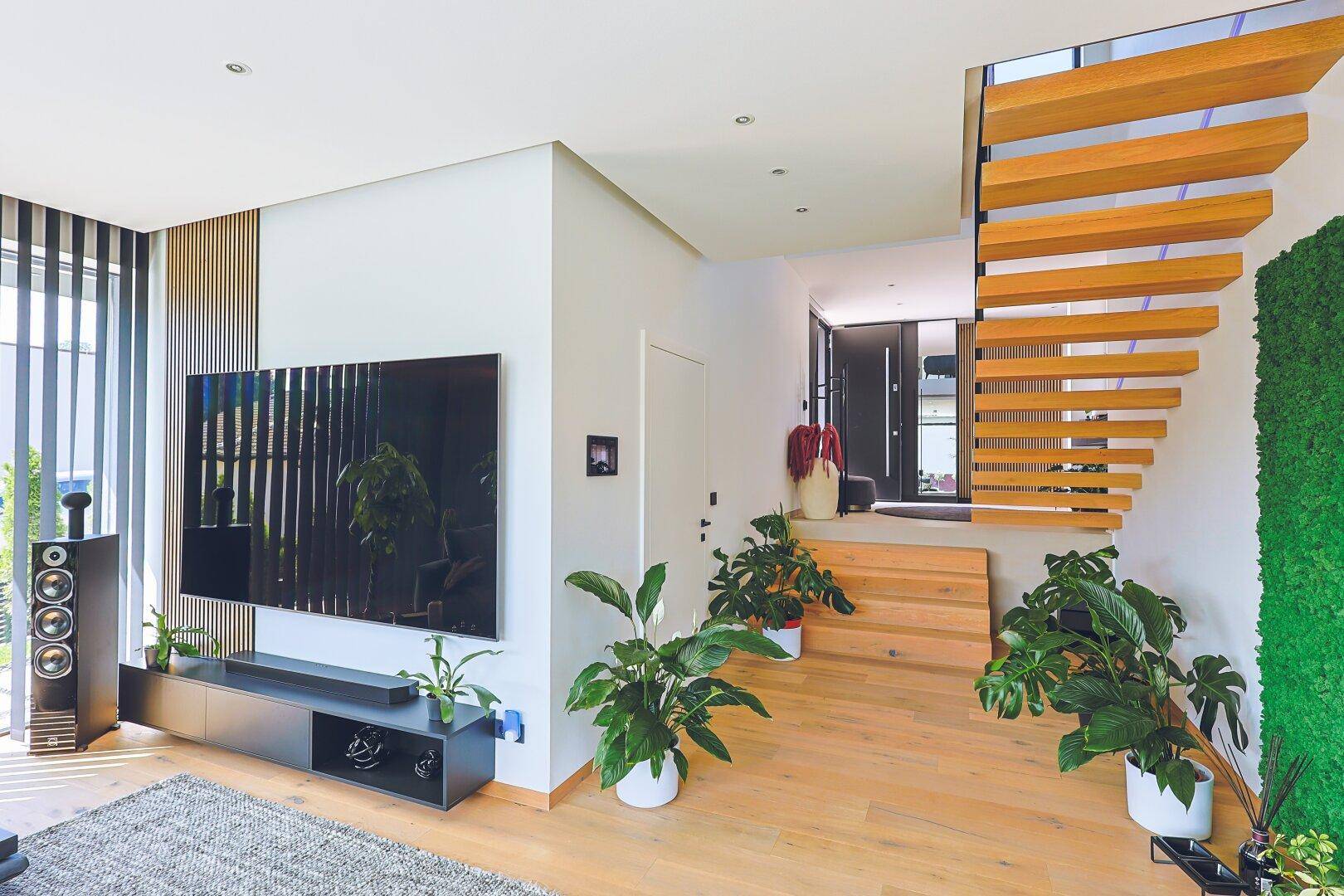 Heller Eingangsbereich mit moderner Holztreppe und großem Fernseher.