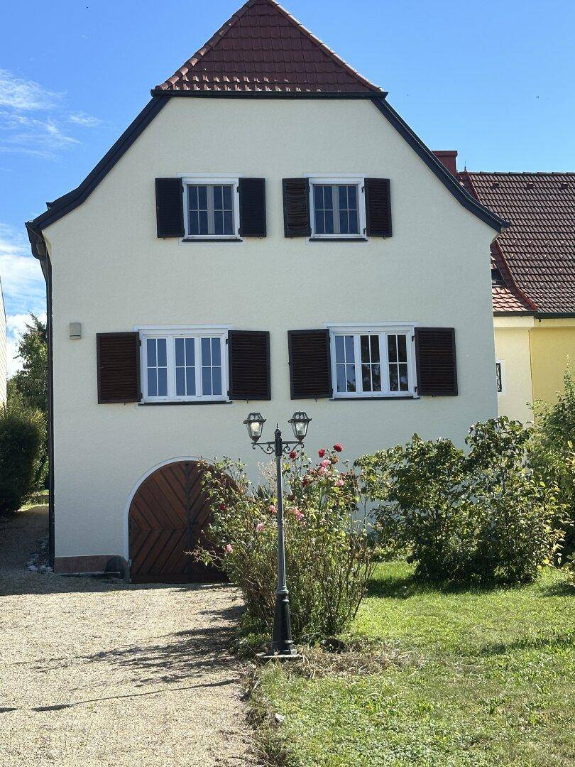 Traditionelles Haus mit markantem Dach, mehreren Fenstern mit Fensterläden und einer Holzgaragentür.