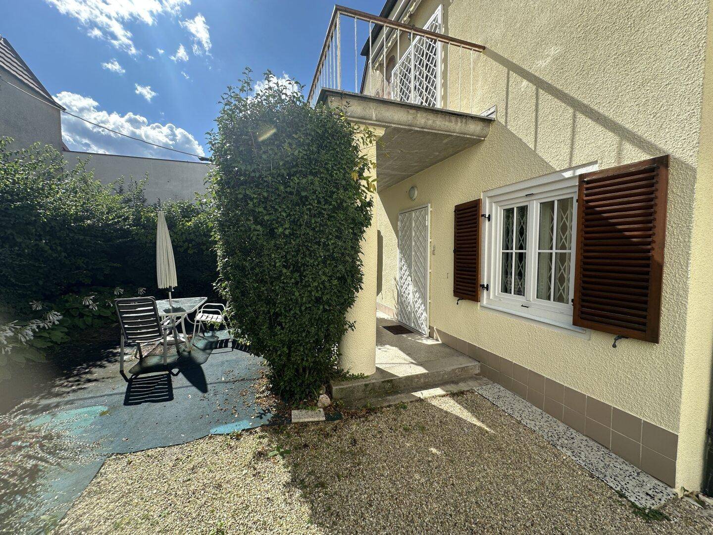 Außenbereich des Hauses mit einer kleinen Terrasse, Gartenmöbeln und einem Balkon im Obergeschoss.