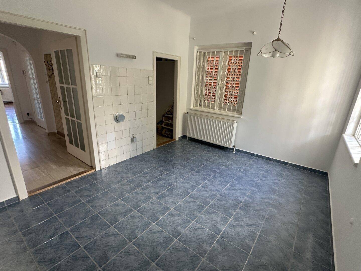 Küche oder Hauswirtschaftsraum mit blauen Fliesen, weiß gefliester Wand und einem Fenster mit Gitter.