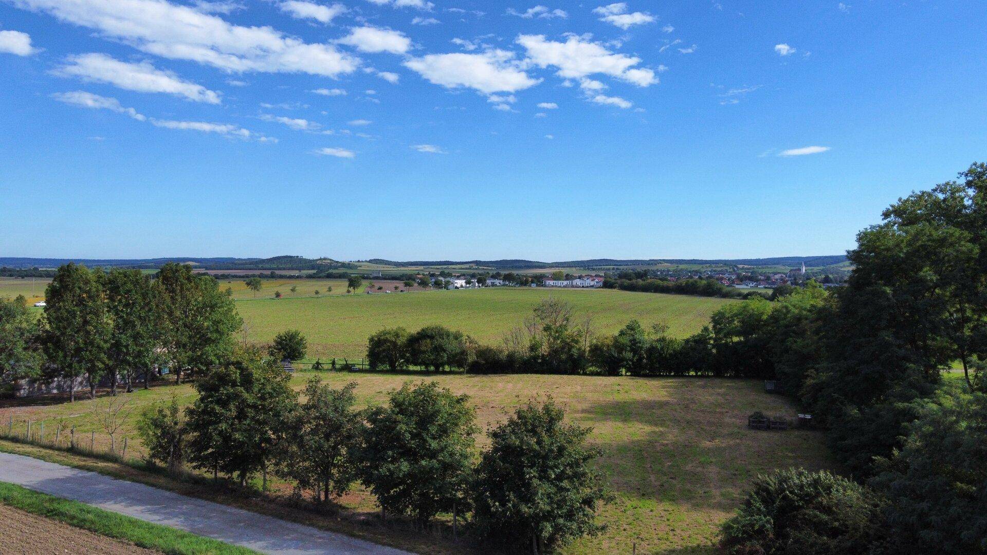 Panoramablick über grüne Felder und eine ländliche Umgebung mit einer Straße im Vordergrund.