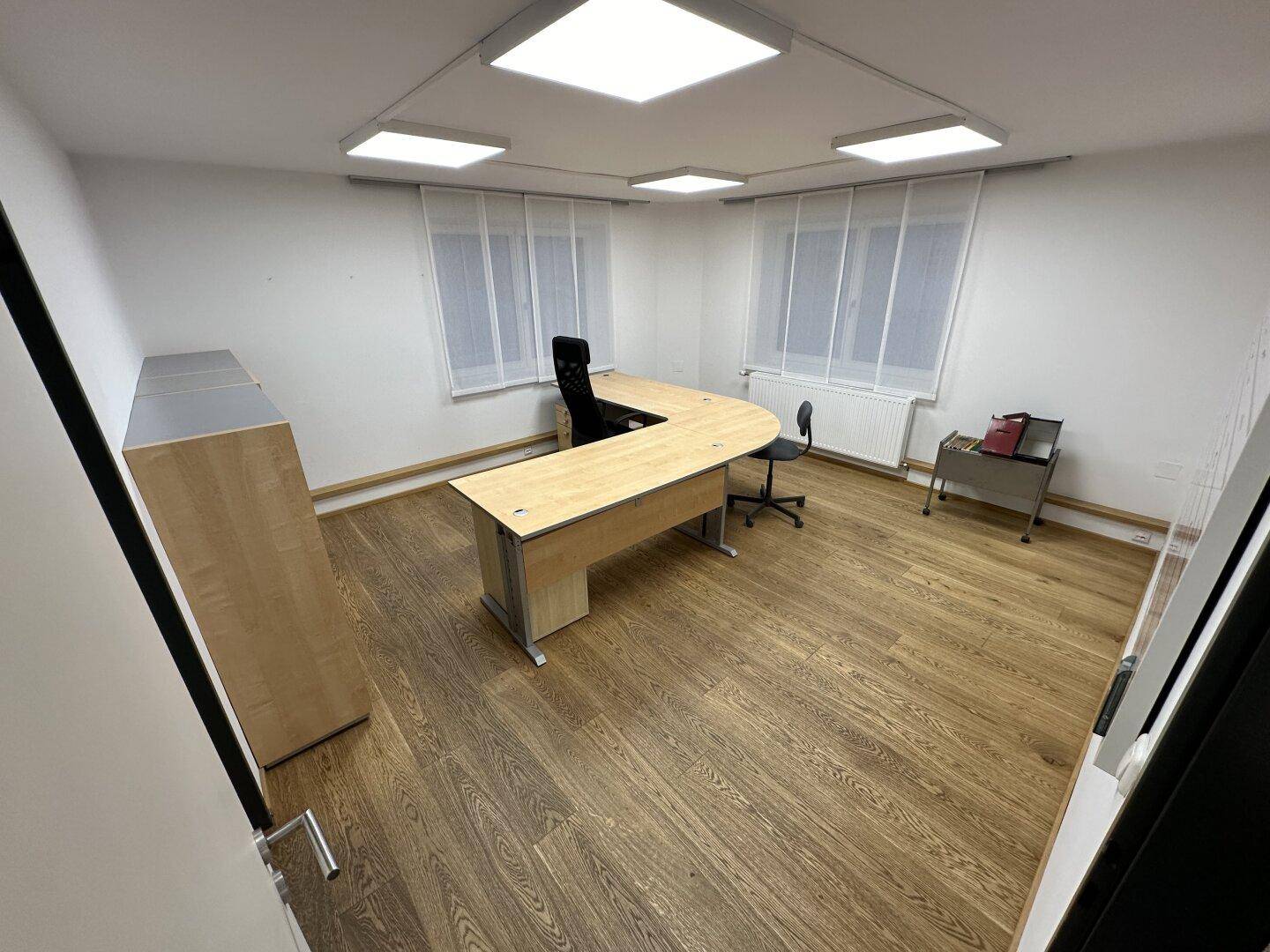 Geräumiges Büro mit Holzboden, U-förmigem Schreibtisch und mehreren Fenstern für viel Tageslicht.
