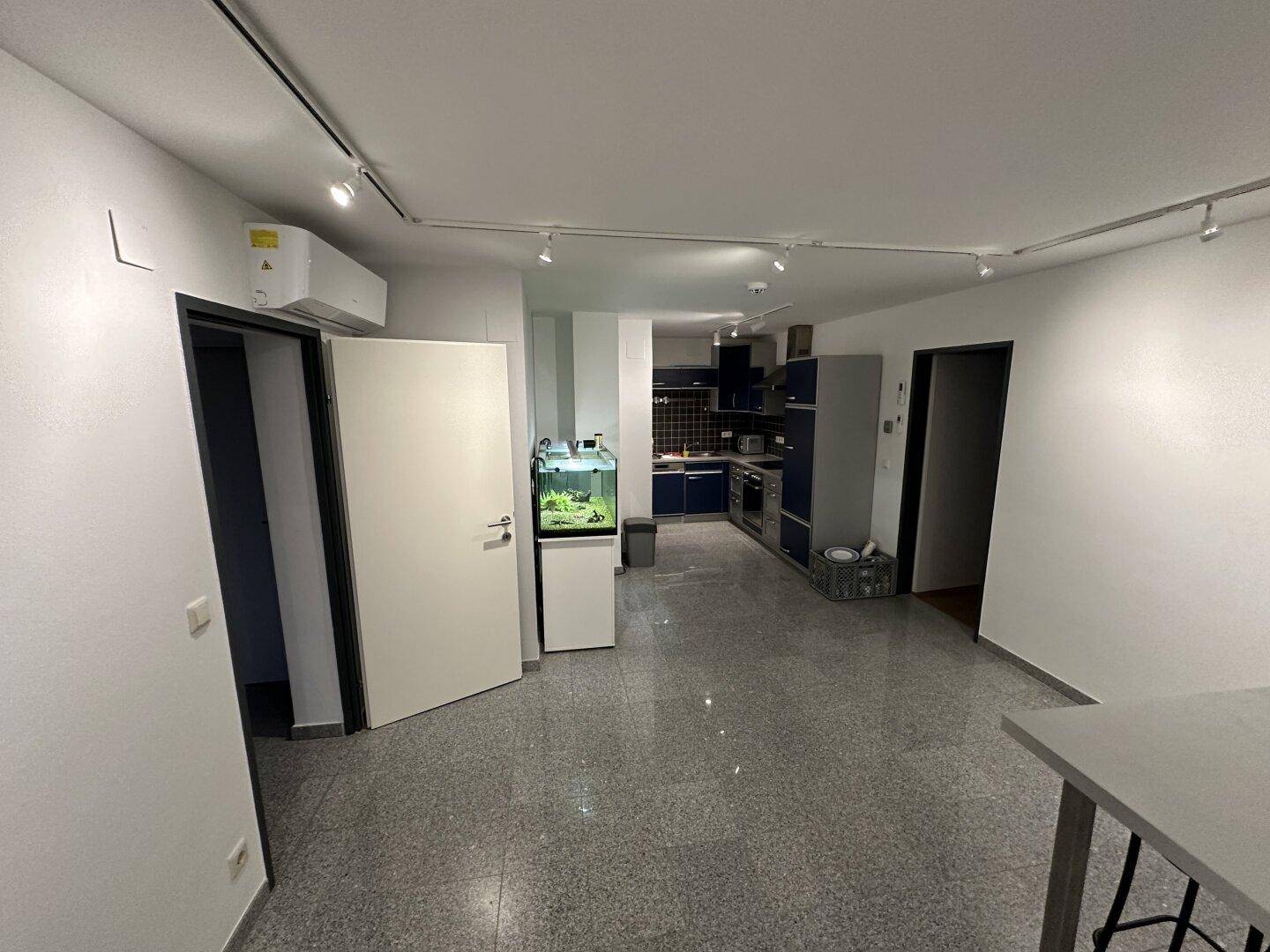 Offener Bereich mit moderner Küche, grauem Fliesenboden, Klimaanlage und einem Aquarium.