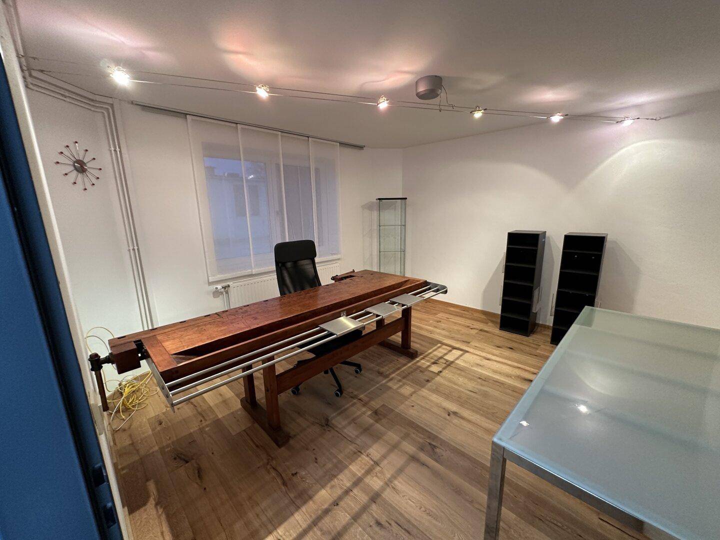 Arbeitszimmer oder Büro mit Holzboden, großer Werkbank, Glastisch und Schienenbeleuchtung.