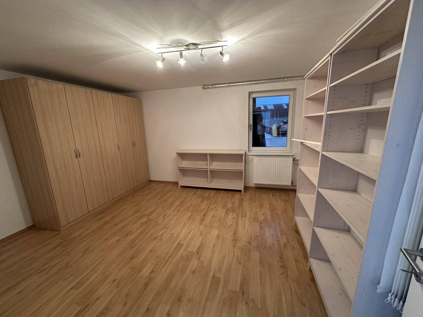 Raum mit Holzboden, weißen Wänden, großem Kleiderschrank und offenen Regalen.