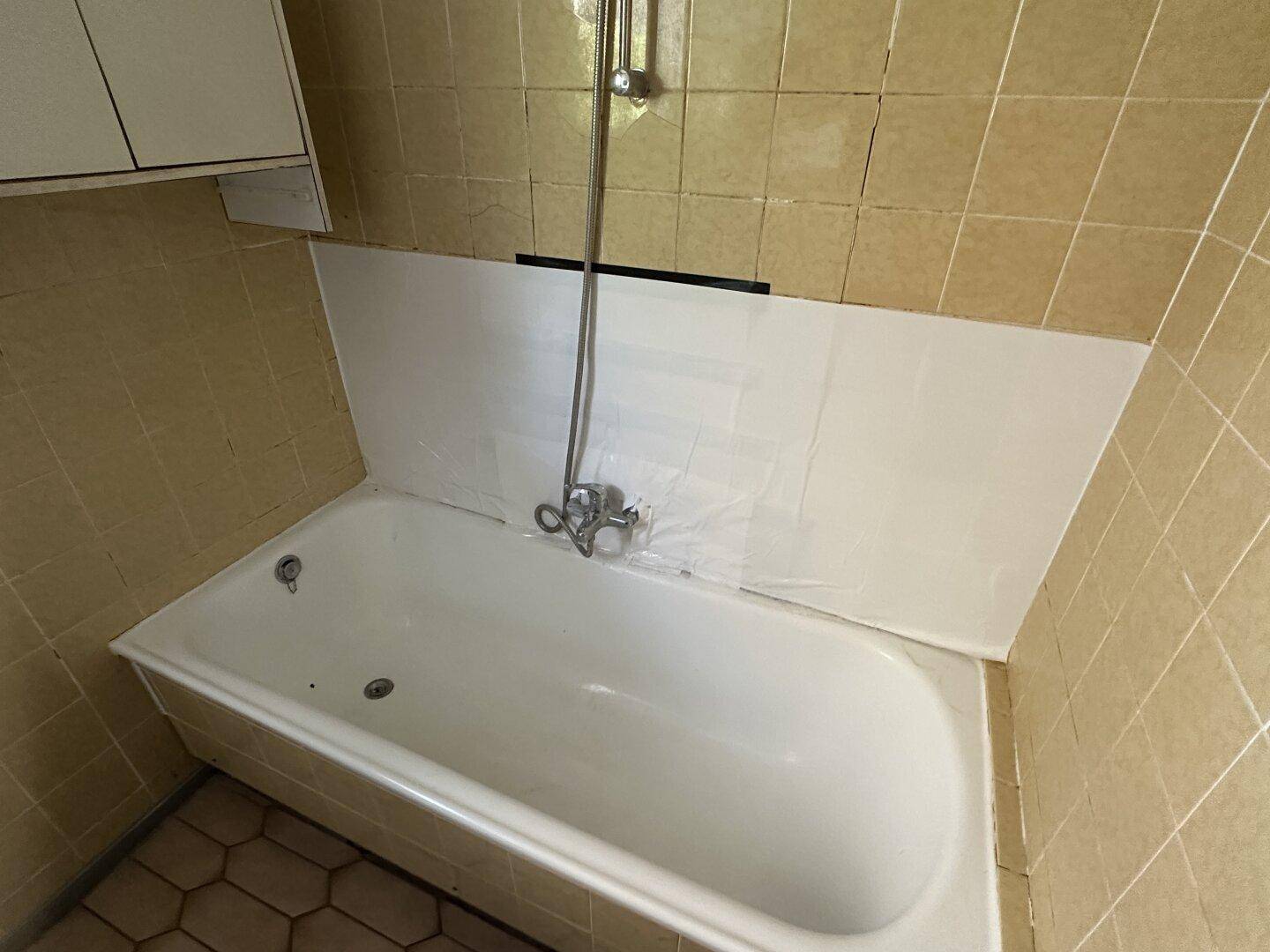 Badezimmer mit Badewanne und beigefarbenen Fliesen, das eine Renovierung benötigt.