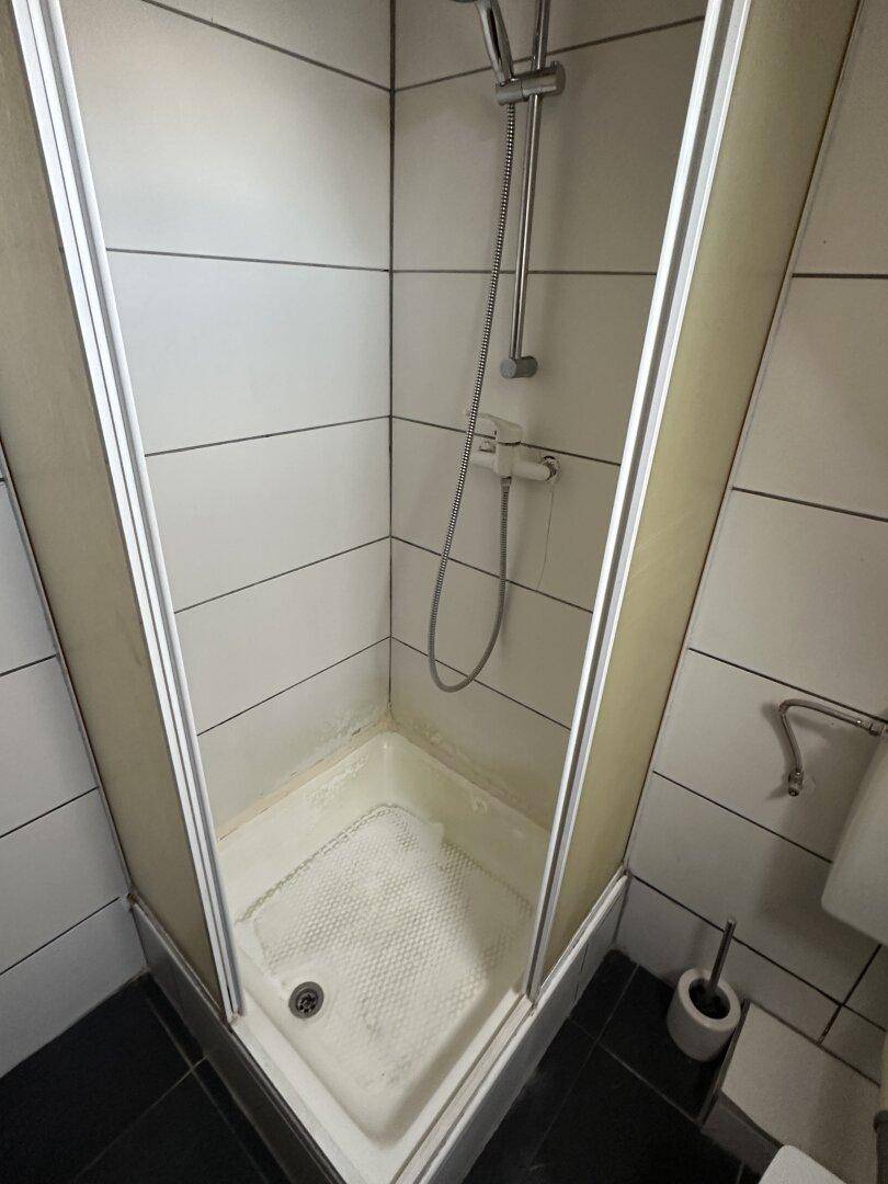 Duschkabine in einem Badezimmer mit weißen und schwarzen Fliesen, das eine Auffrischung benötigt.
