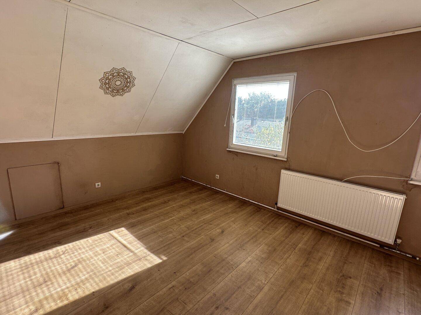 Weiteres Dachzimmer mit Laminatboden, braunen Wänden und einem Fenster, das renoviert werden muss.