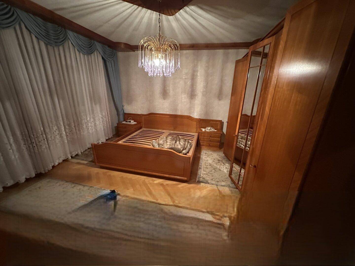 Schlafzimmer mit Holzbett, Nachttischen und einem eleganten Kronleuchter.