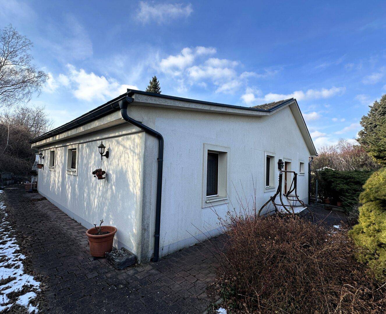 Seitenansicht des Hauses mit gepflastertem Weg und winterlicher Vegetation im Garten.