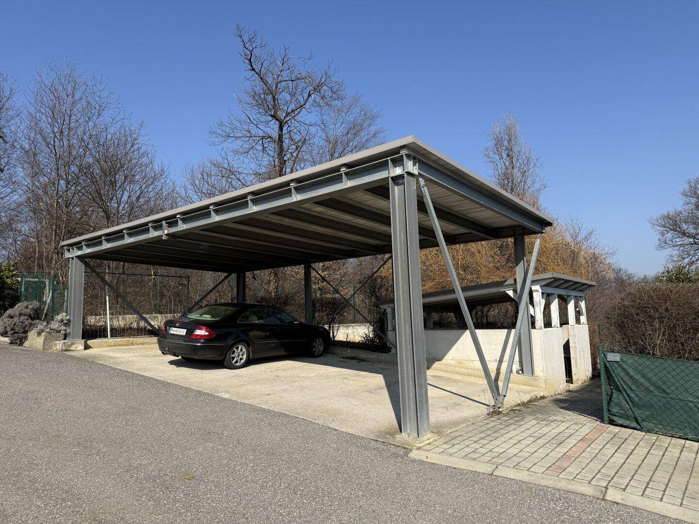 Überdachter Carport mit Stellplatz für ein Fahrzeug, umgeben von Bäumen.