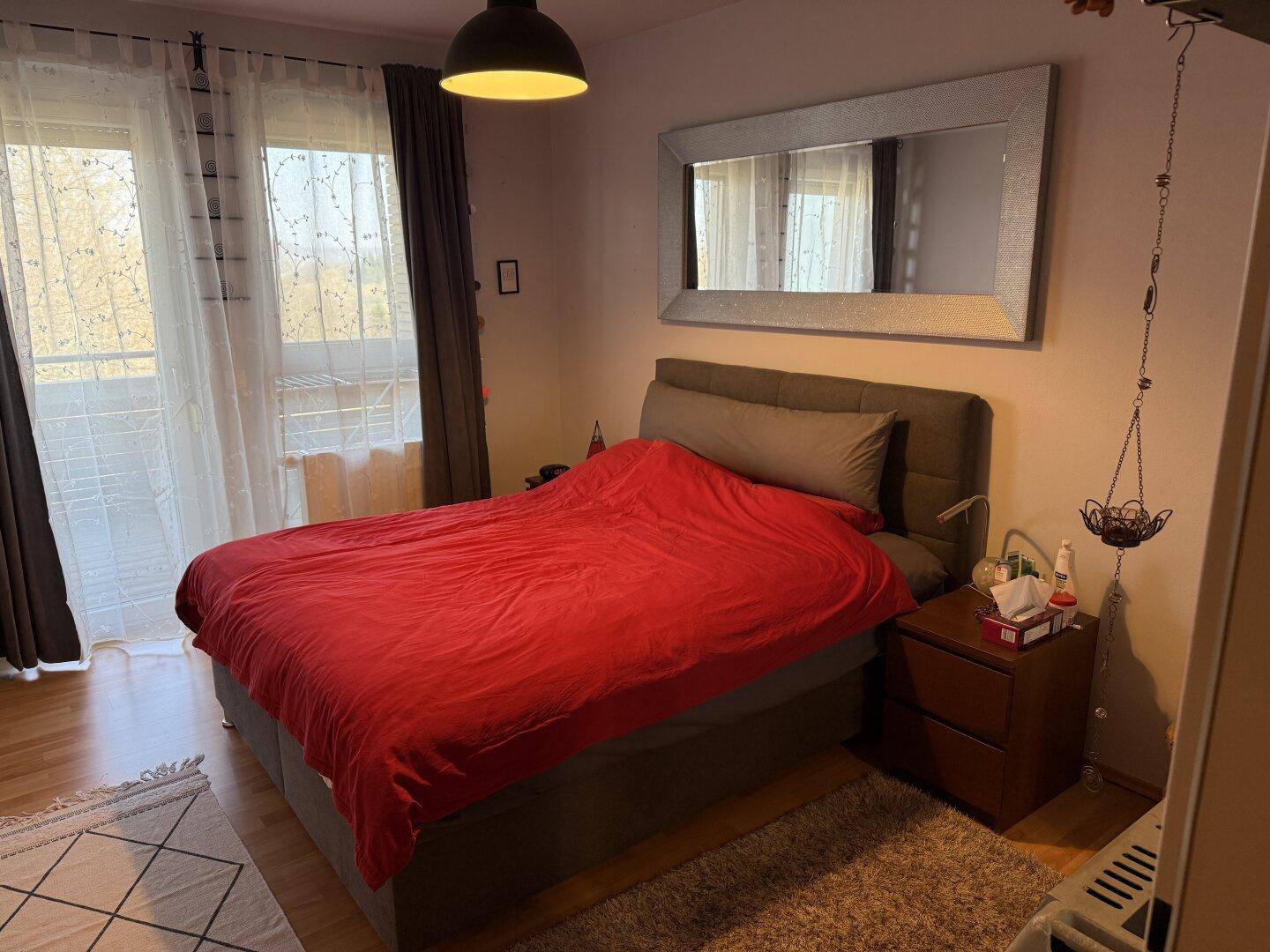 Schlafzimmer mit Doppelbett, Parkettboden und Zugang zu einem Balkon.