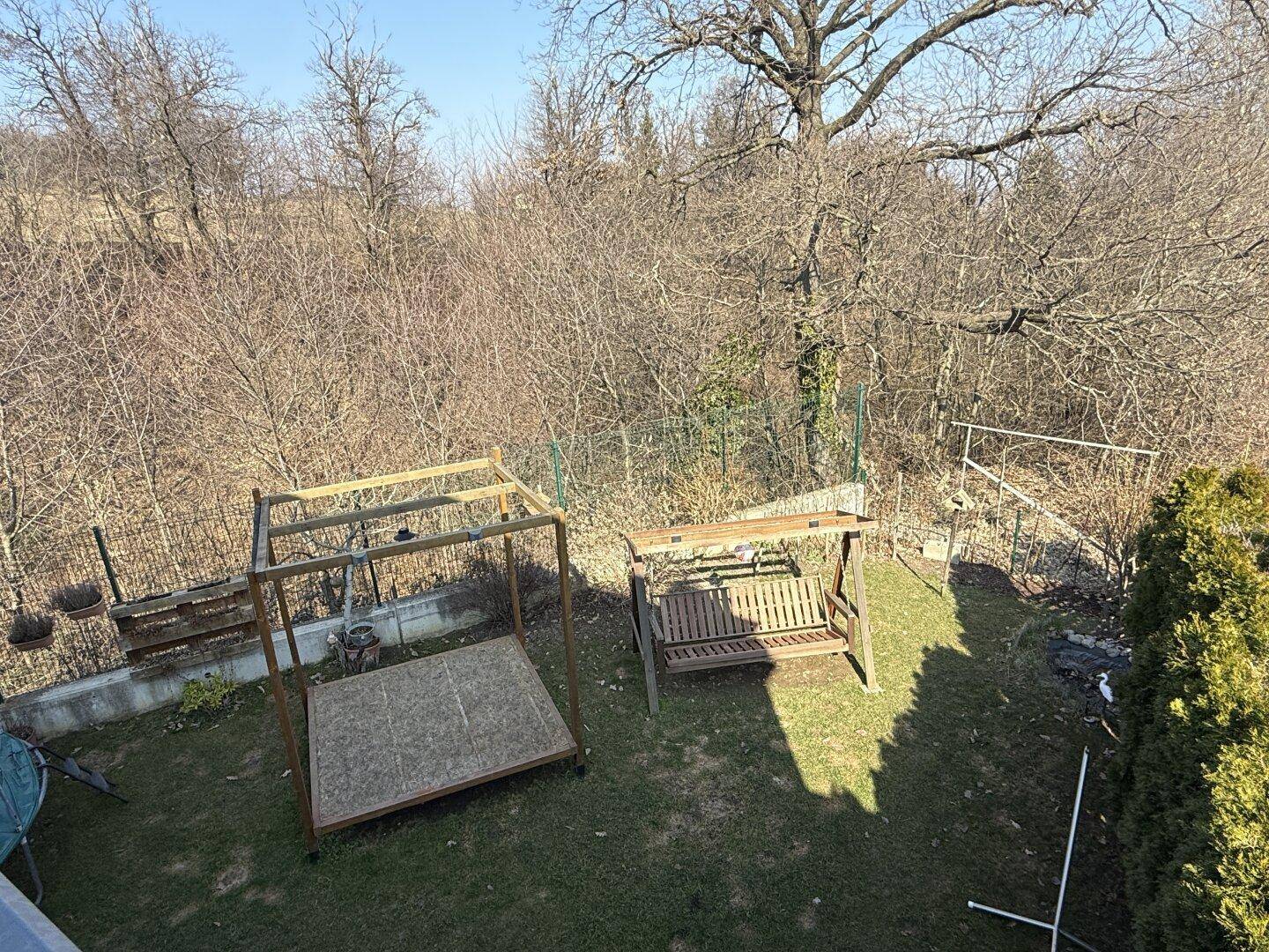 Überblick über den Garten mit Schaukel und Liegefläche, umgeben von Bäumen.