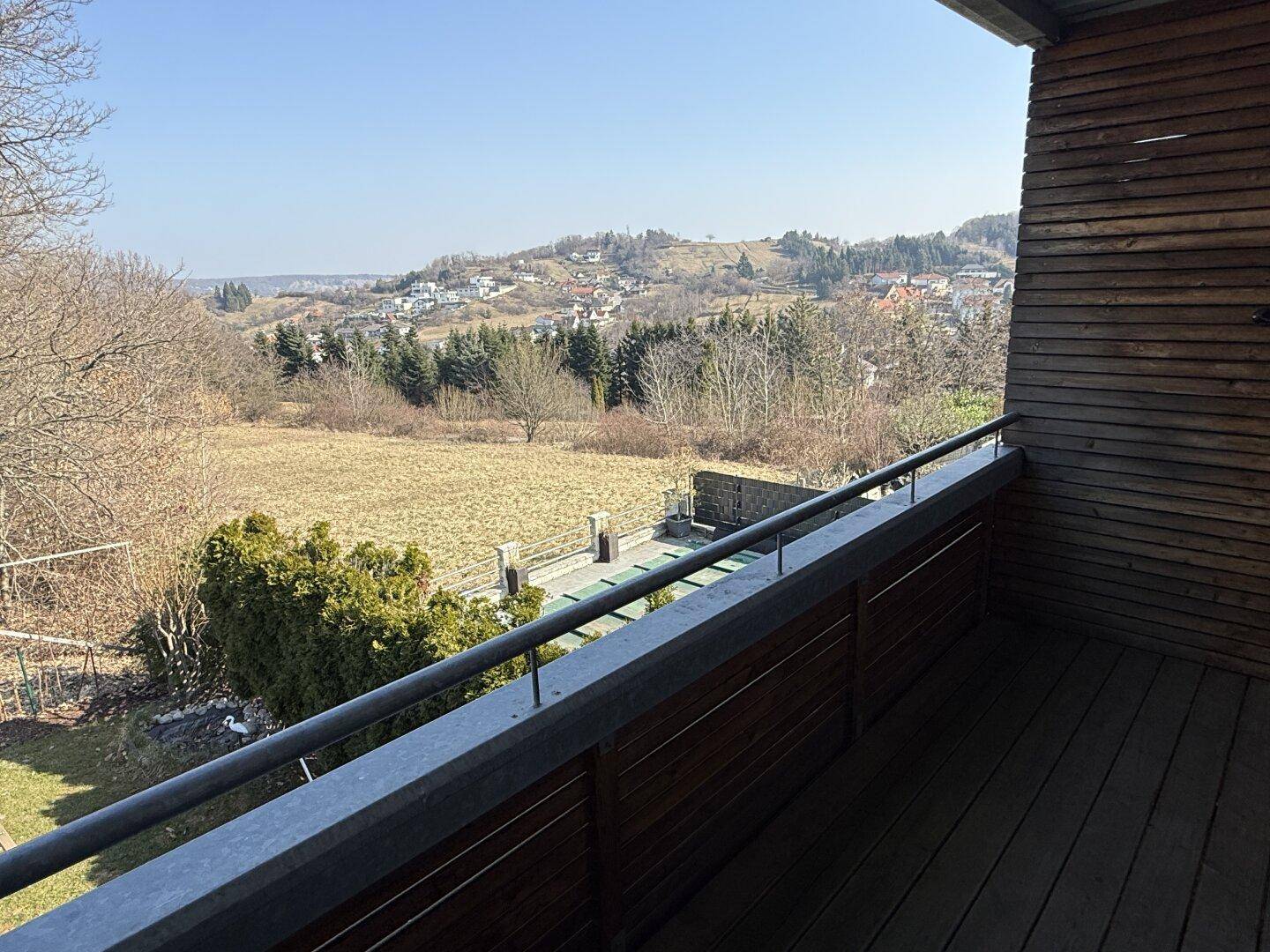 Balkon mit Holzboden und weitem Blick über die grüne Landschaft und umliegende Häuser.