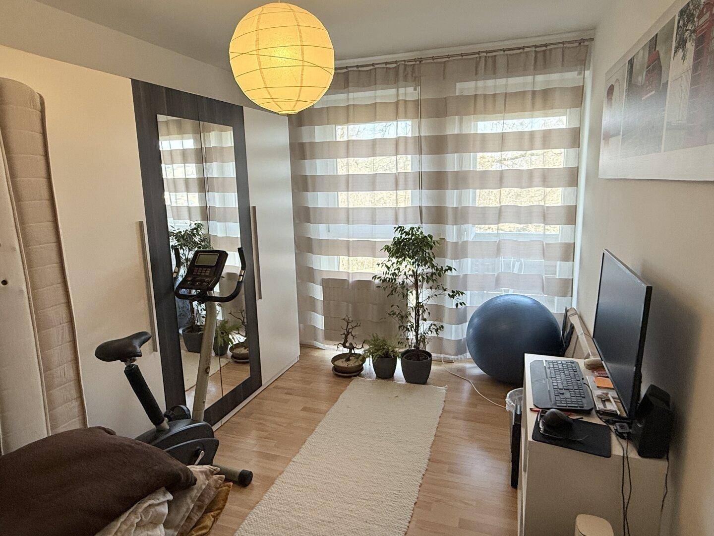 Helles Zimmer mit Parkettboden, Kleiderschrank und Fitnessgerät, ideal als Gäste- oder Arbeitszimmer.
