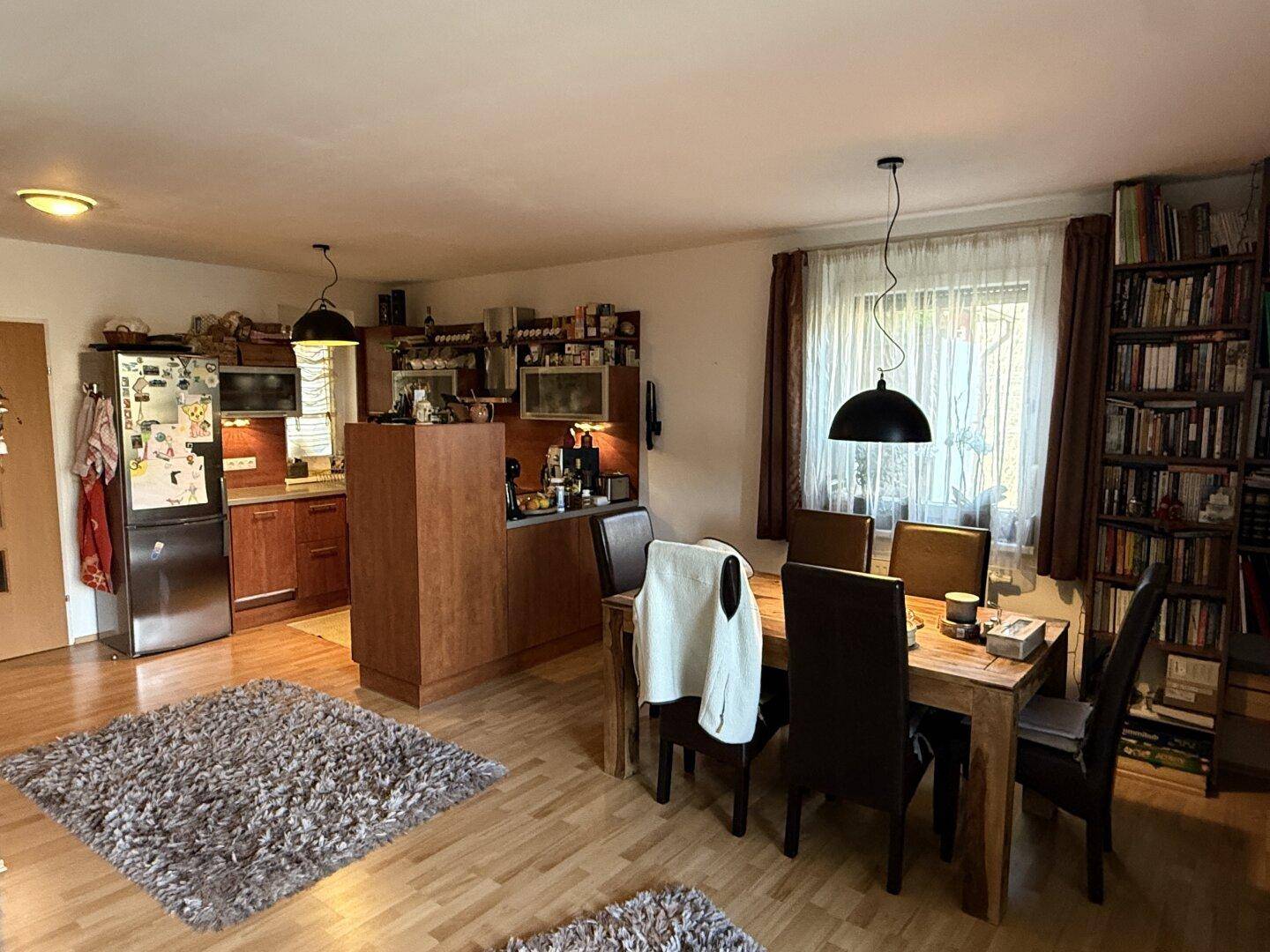 Offener Wohn- und Essbereich mit Holztisch, Parkettboden und integrierter Küche.