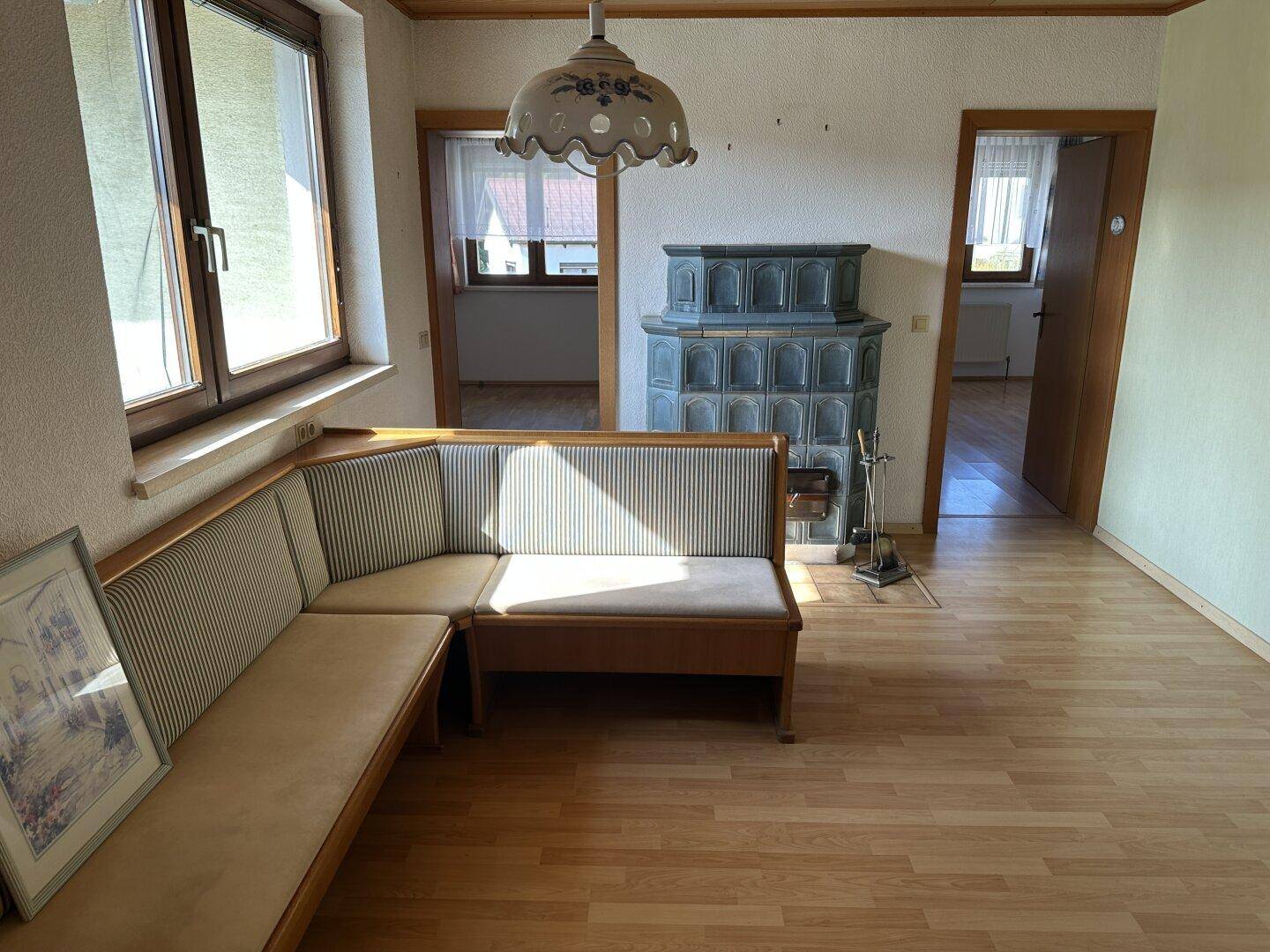 Helles Wohnzimmer mit Kachelofen, Laminatboden und traditioneller Sitzecke.