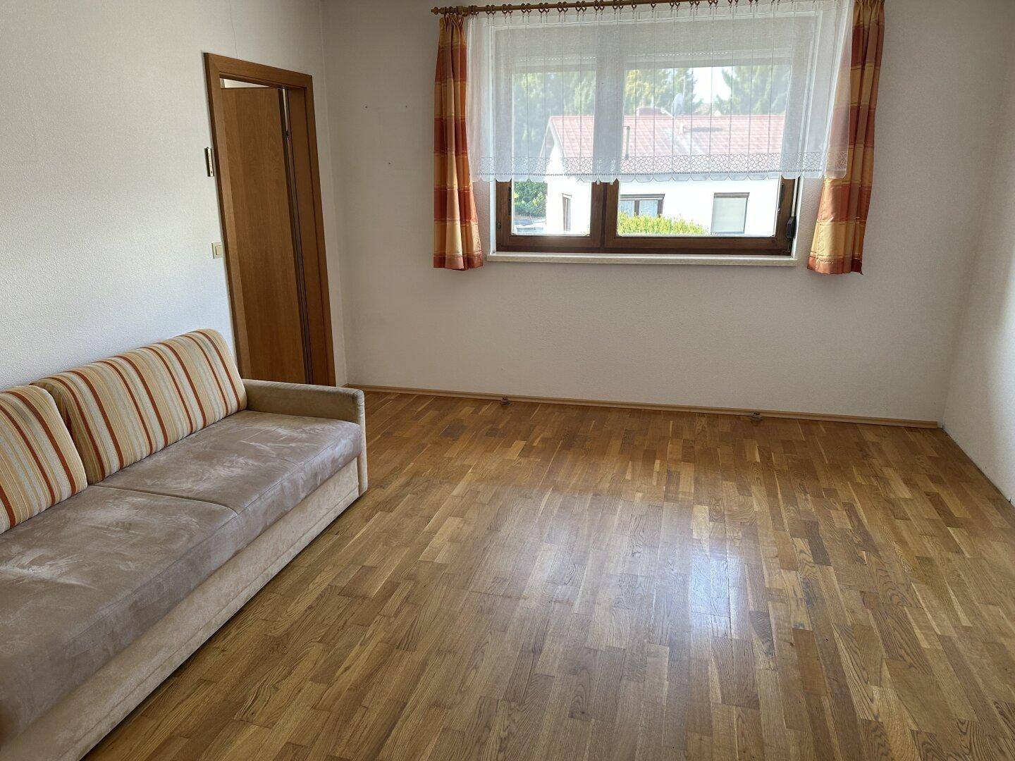 Helles Zimmer mit Holzboden und einem Sofa, ideal als Wohn- oder Schlafzimmer.