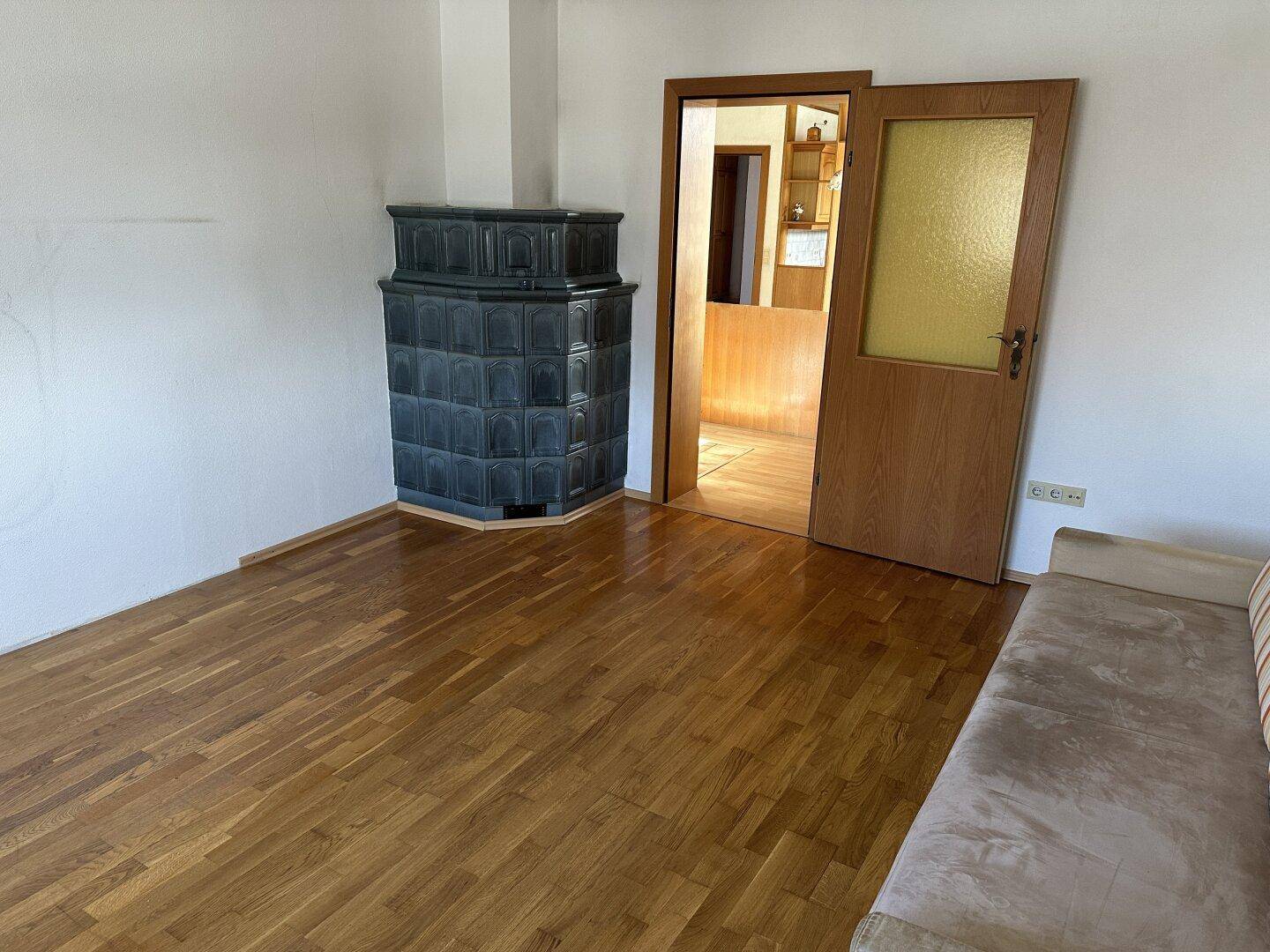 Gemütliches Zimmer mit Kachelofen, Holzboden und Sofa.