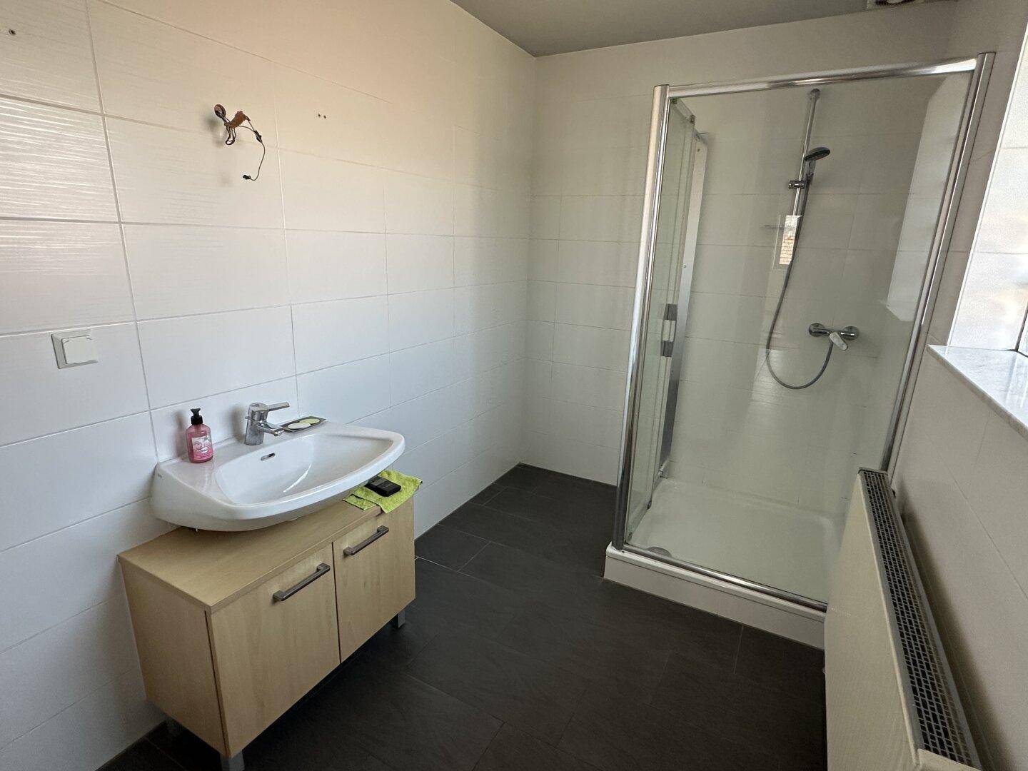 Modernes Badezimmer mit Dusche, Waschbecken und weißen Fliesen.