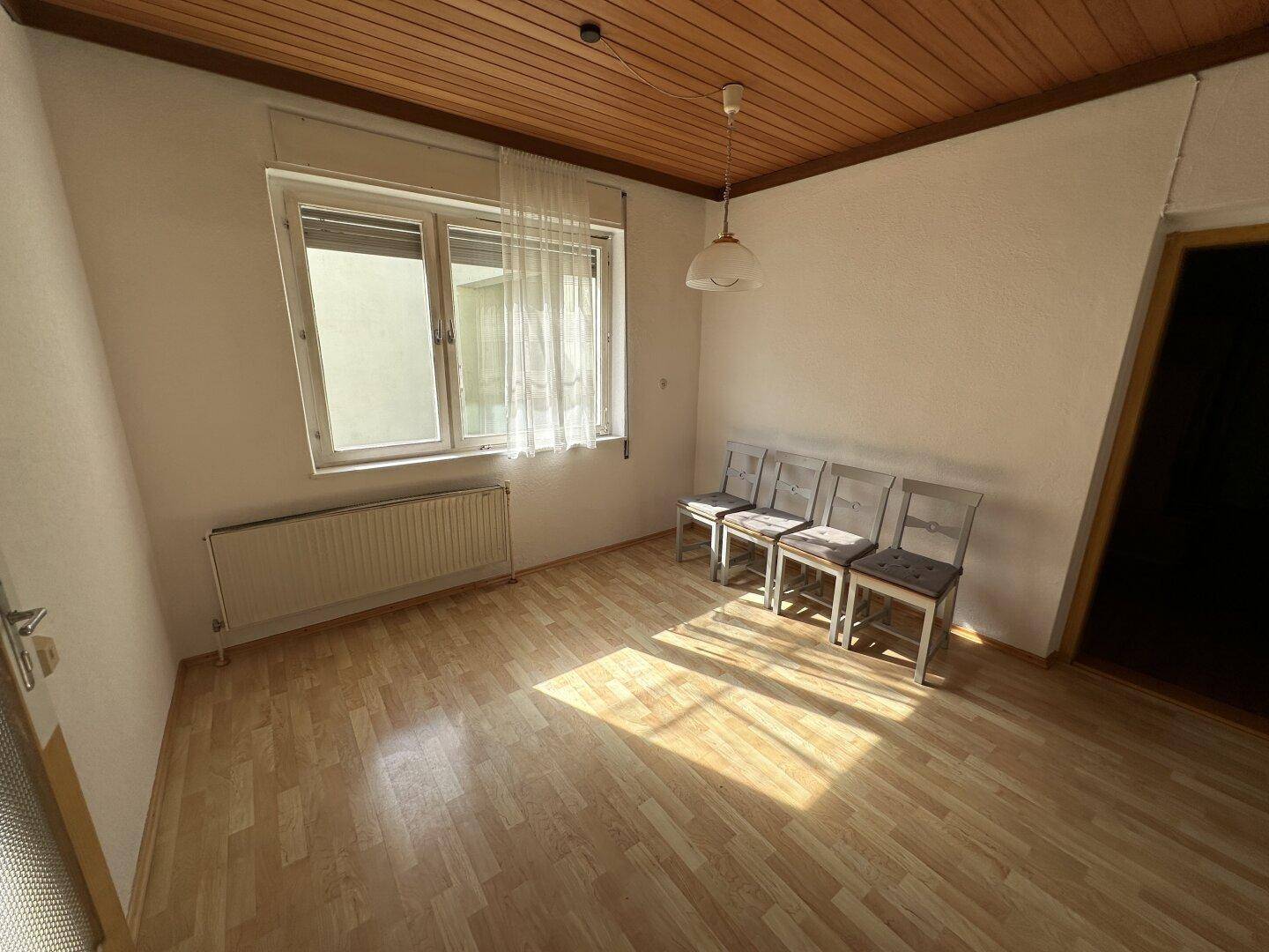 Helles Zimmer mit Laminatboden, Holzdecke und Fenster, geeignet als Esszimmer.