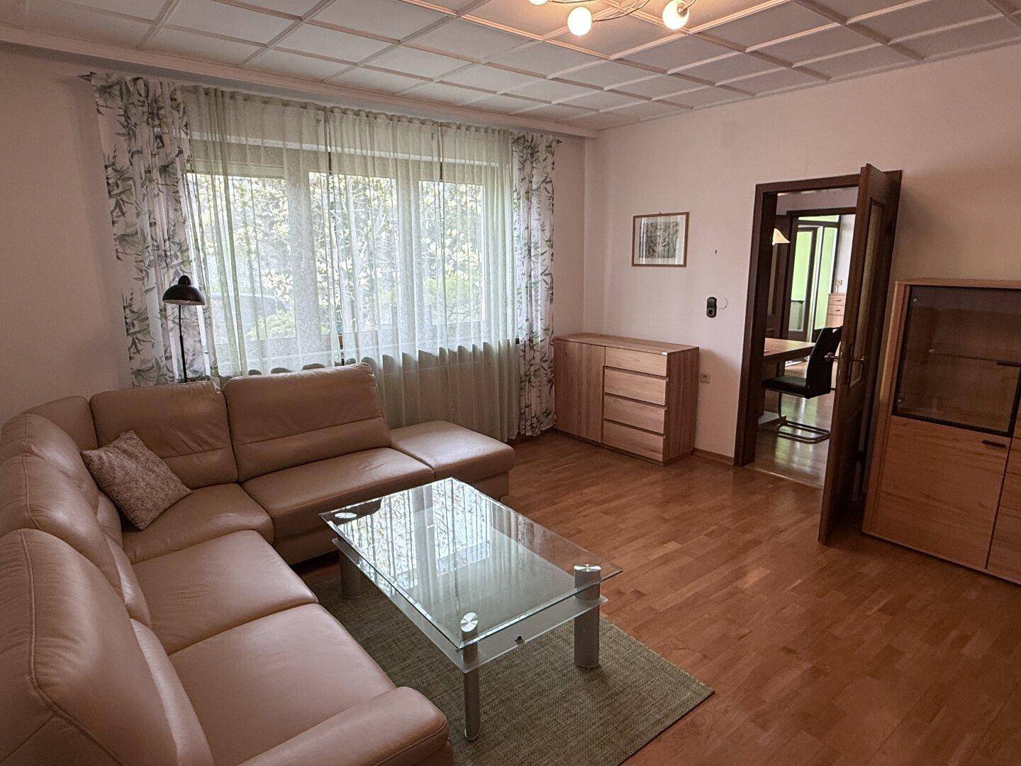 Geräumiges Wohnzimmer mit Ecksofa, Laminatboden und Blick in den angrenzenden Flur.