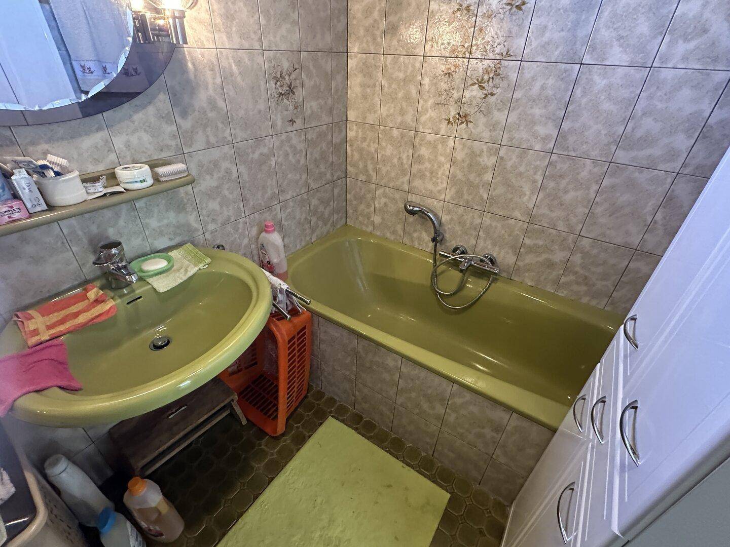Badezimmer im Stil der 80er Jahre mit grüner Badewanne, passendem Waschbecken und Wandfliesen.