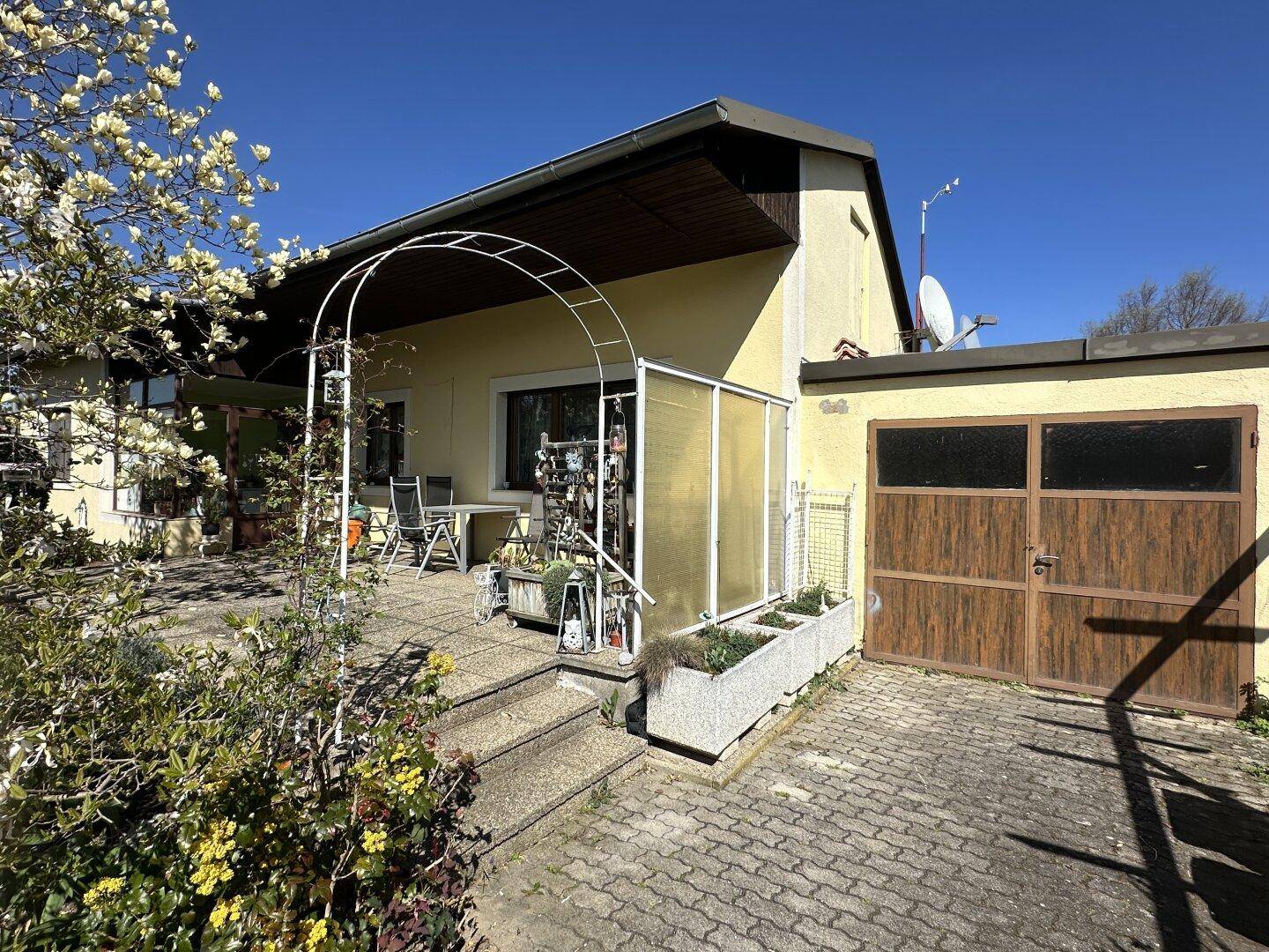Sonniger Terrassenbereich vor dem Haus mit Sitzgelegenheiten und Zugang zum Garten.